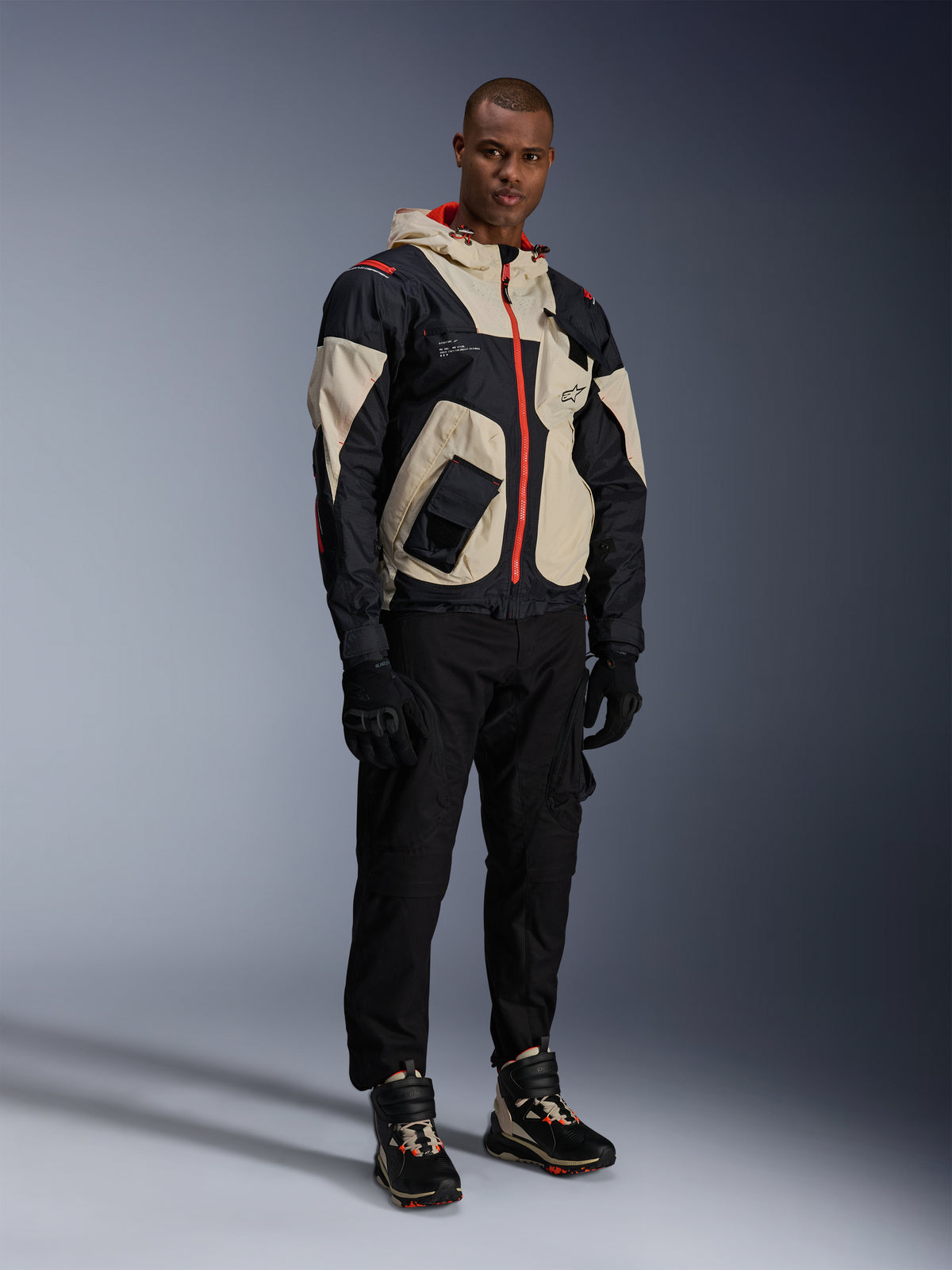 Man standing in full urban motorcycle gear, featuring Alpinestars Speedstreet Shoes in Black Almond Hot Orange and a Mogress Air Jacket in black and cream, coordinated black pants and gloves, streetwear-inspired protective outfit for street riding