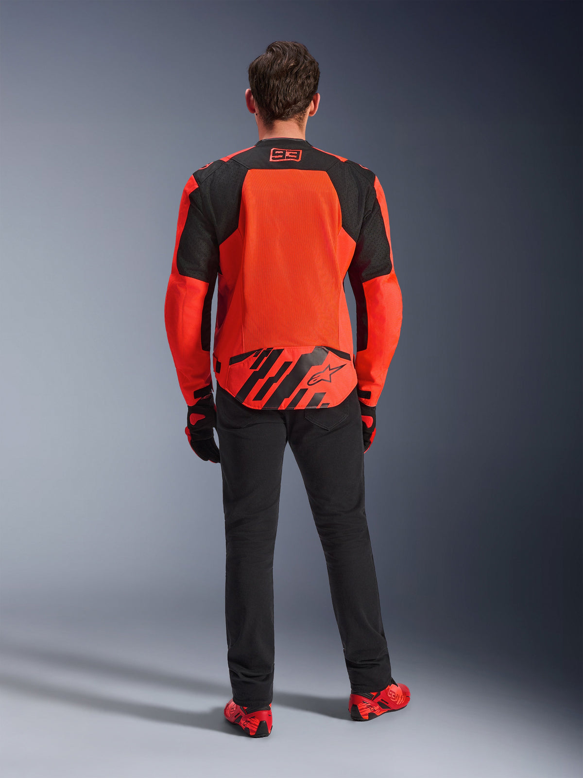 Rückansicht der MM93 T-SPS Air V2 Jacke, Rot Fluo und Schwarz, Textil-Motorradjacke mit großen Mesh-Panels auf dem Rücken zur Belüftung, getragen mit einer schwarzen Hose und rotem Schuhwerk, mit Marc Marquez 93 Branding