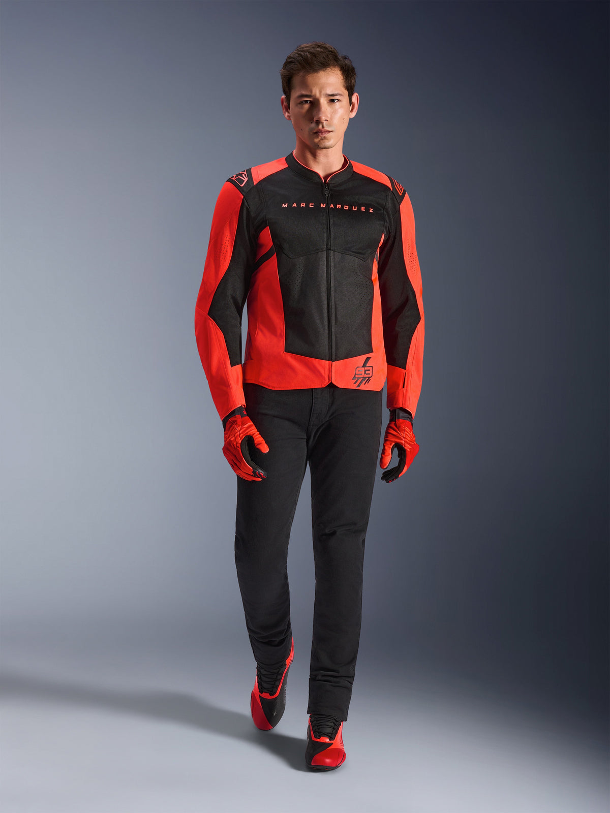 Alpinestars MM93 T-SPS Air V2 Jacke, Rot Fluo und Schwarz, getragen von einem Model mit passenden roten Handschuhen und schwarzer Hose, mit Marc Marquez Branding und dem 93-Logo, belüftete Sport-Motorradjacke für die Stadt