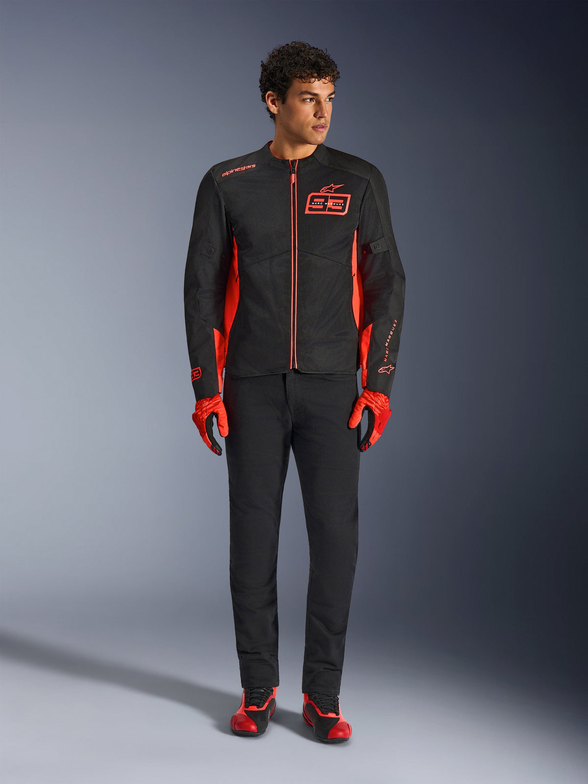 Alpinestars MM93 C-1 Air Jacke, Motorradjacke, Schwarz und Fluo-Rot, mit Marc Marquez Branding und 93-Logo, getragen von einem Model mit passenden roten Handschuhen und schwarzer Hose, leichte Textil- und Mesh-Konstruktion für den urbanen Einsatz
