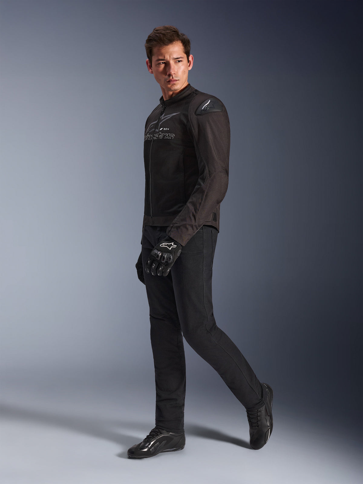Alpinestars SMX Air Jacke in Schwarz Anthrazit, getragen von einem Model mit passender schwarzer Motorradhose, Handschuhen und Schuhen, Studio-Ganzkörperaufnahme, Performance-Sport-Motorradausrüstung mit Tech-Mesh und Schulter-Slidern