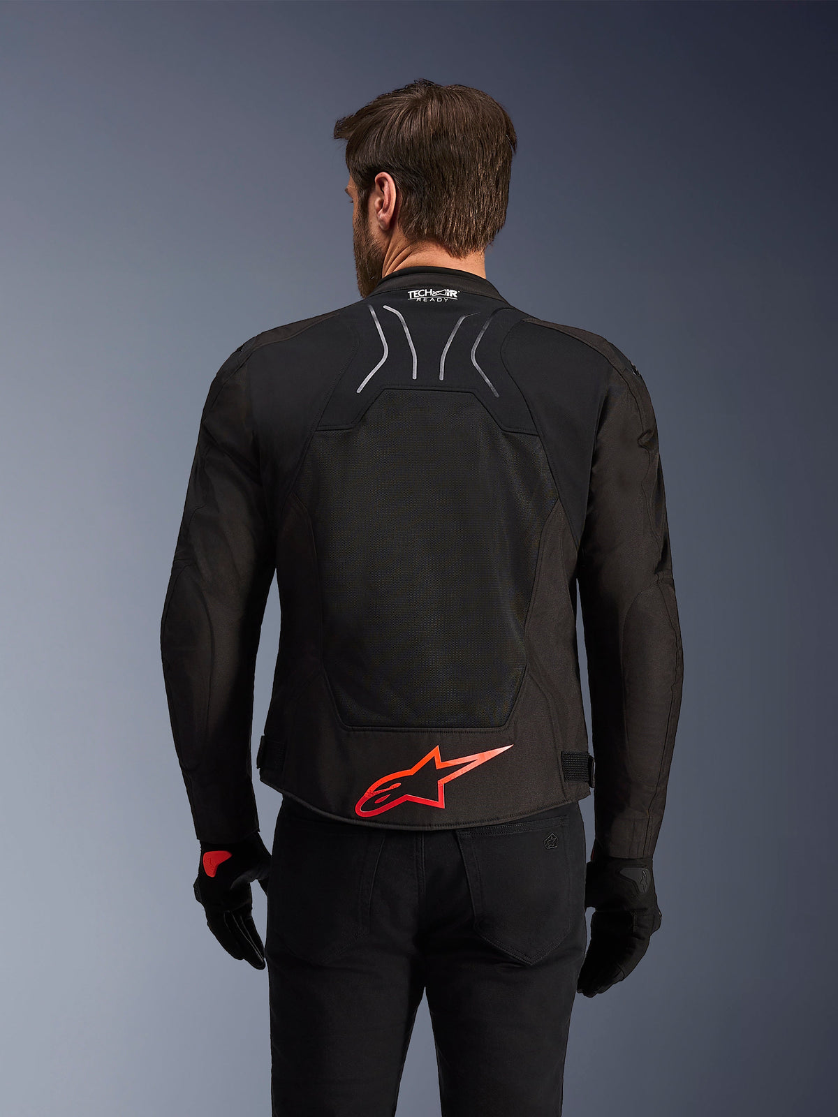 Alpinestars SMX Air Jacke, Rückansicht, Schwarz mit leuchtend rotem Alpinestars-Logo am unteren Rücken, mit High-Airflow-Tech-Mesh-Einsatz und Tech-Air-Ready-Branding, getragen von einem männlichen Fahrer mit schwarzer Hose und Handschuhen