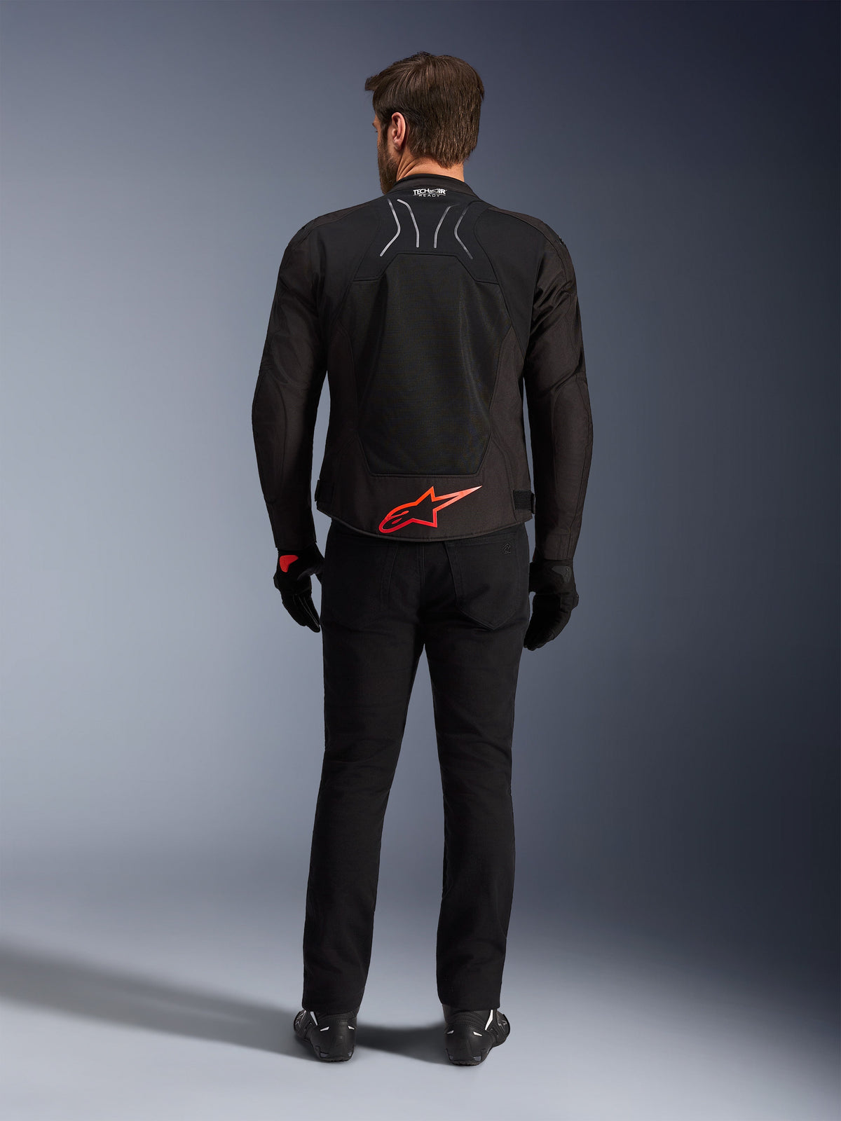 Alpinestars SMX Air Jacke, Schwarz mit leuchtend rotem Logo, Rückansicht mit Tech-Air Ready Branding und Mesh-Belüftungseinsätzen, getragen mit schwarzer Hose und Handschuhen, Hochleistungs-Sport- und Rennmotorrad-Ausrüstung