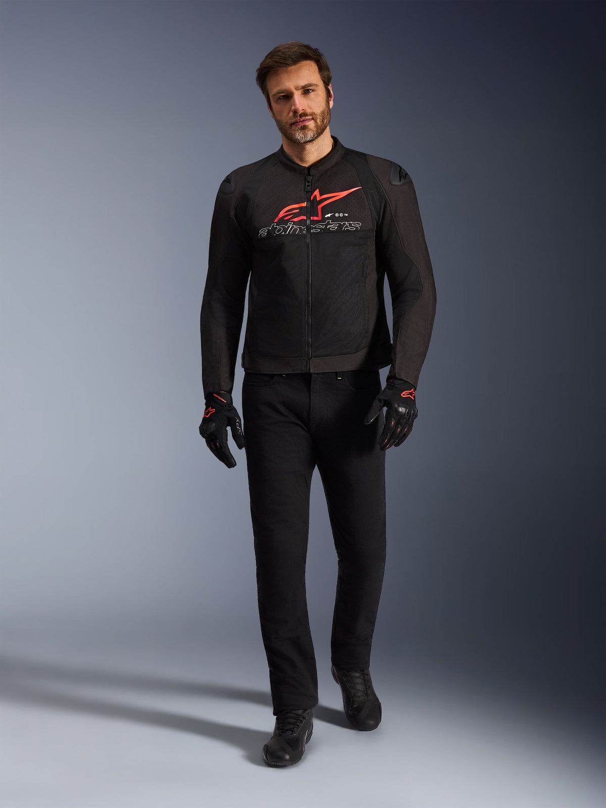 Alpinestars SMX Air Jacke, Schwarz, Leuchtendes Rot und Weiß, sportliche Motorradjacke getragen mit schwarzer Motorradhose und Handschuhen, mit technischen Mesh-Einsätzen und markantem rotem Alpinestars-Logo auf der Brust, Performance-Street-Riding-Outfit