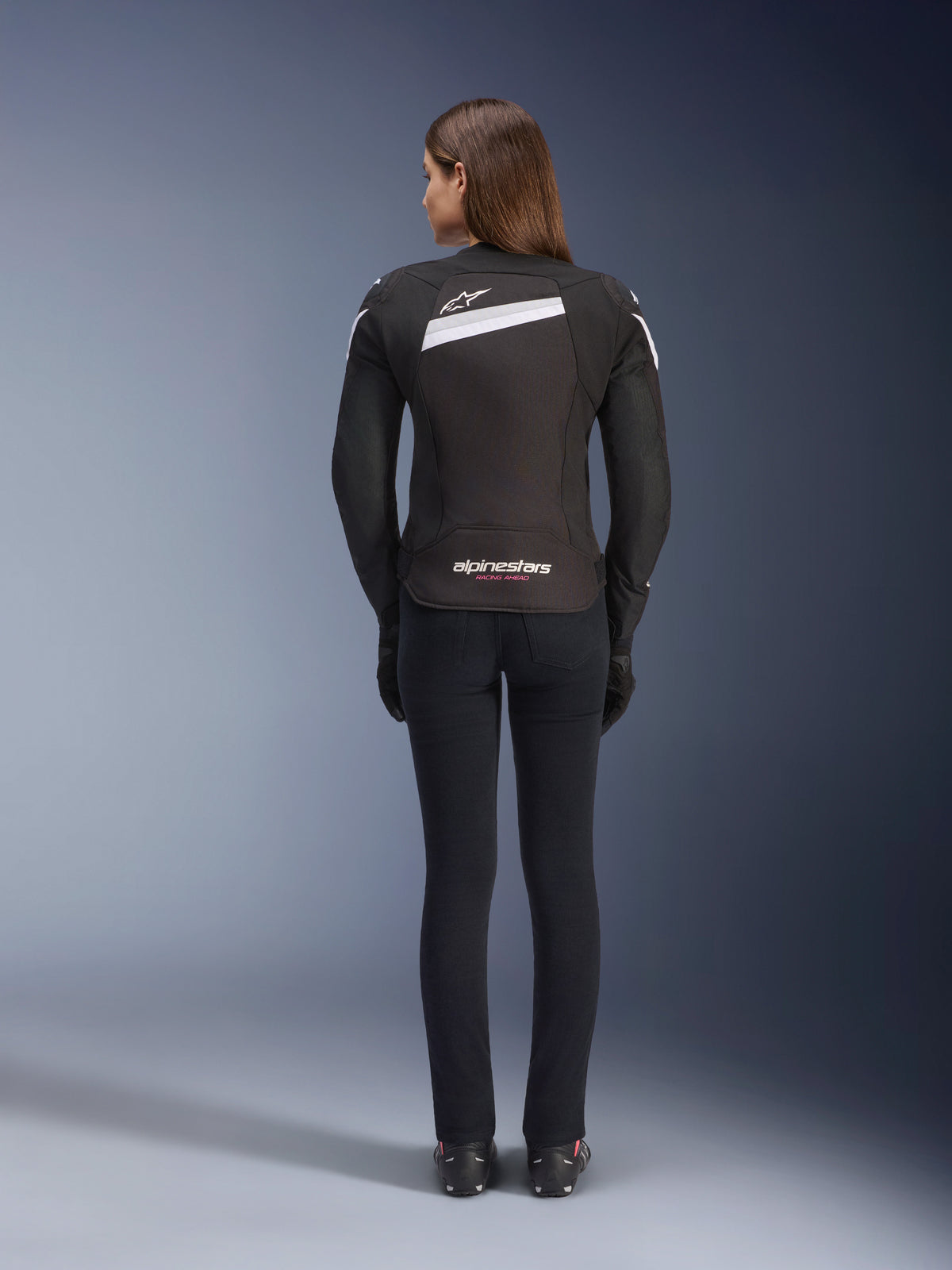 Alpinestars Stella T-GP Plus R V4 Jacke, Textil-Motorradjacke für Damen, Schwarz und Weiß, Rückansicht mit weißen Akzenten und Logo-Branding auf dem Rücken, getragen mit schwarzer Hose, schlanke Sport-Passform für Straßen-Performance