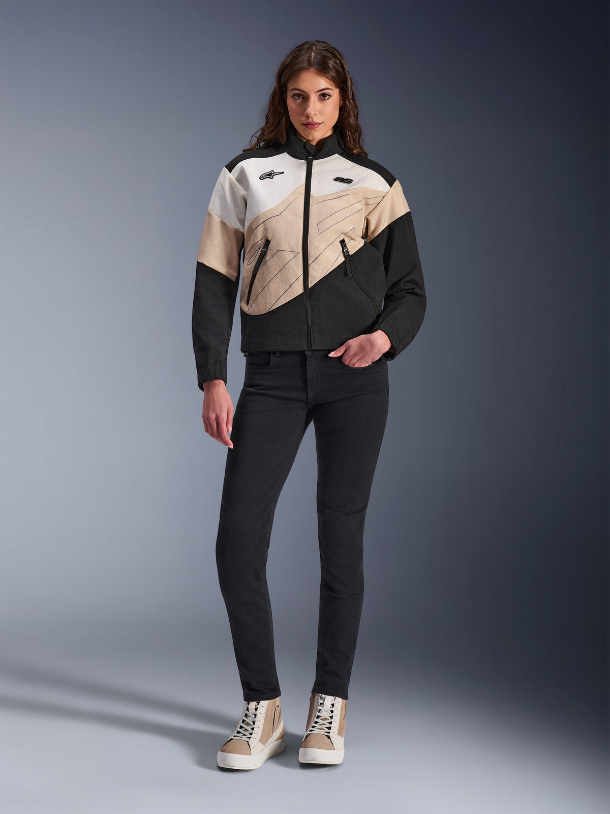 Alpinestars Stella Moshell Damenjacke, urbane Motorradjacke mit asymmetrischem Color-Block-Design in Schwarz, Sand und Off-White, kombiniert mit schwarzer Slim-Fit-Hose und sandfarbenen High-Top-Sneakern, moderne Streetwear-Ästhetik für Fahrerinnen