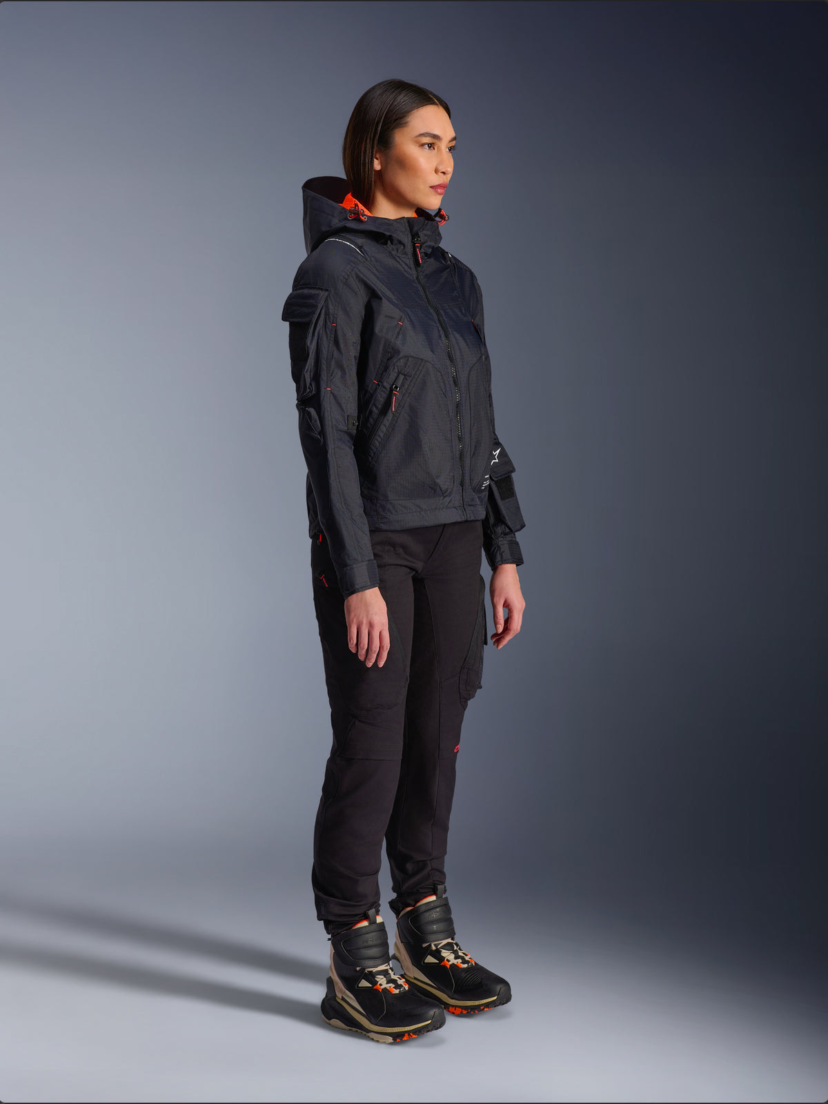 Alpinestars Actea Damen-Hose in Schwarz, reguläre Passform mit Cargotaschen, kombiniert mit einer schwarzen Molly Air Jacke mit orangefarbenen Akzenten und High-Top-Motorradschuhen, moderne urbane Motorradbekleidung für Damen