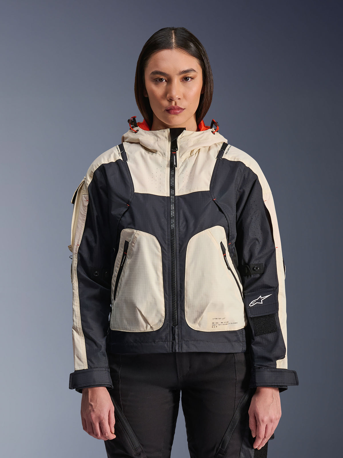 Alpinestars Molly Air Jacke, Urban-Motorradjacke für Damen, Black Almond, Vorderansicht an einem Model, mit cremefarbenen und schwarzen Ripstop-Einsätzen, Kapuze mit orangefarbenem Futter, Reißverschluss vorne und großen Funktionstaschen, moderne, von Streetwear inspirierte Motorradausrüstung