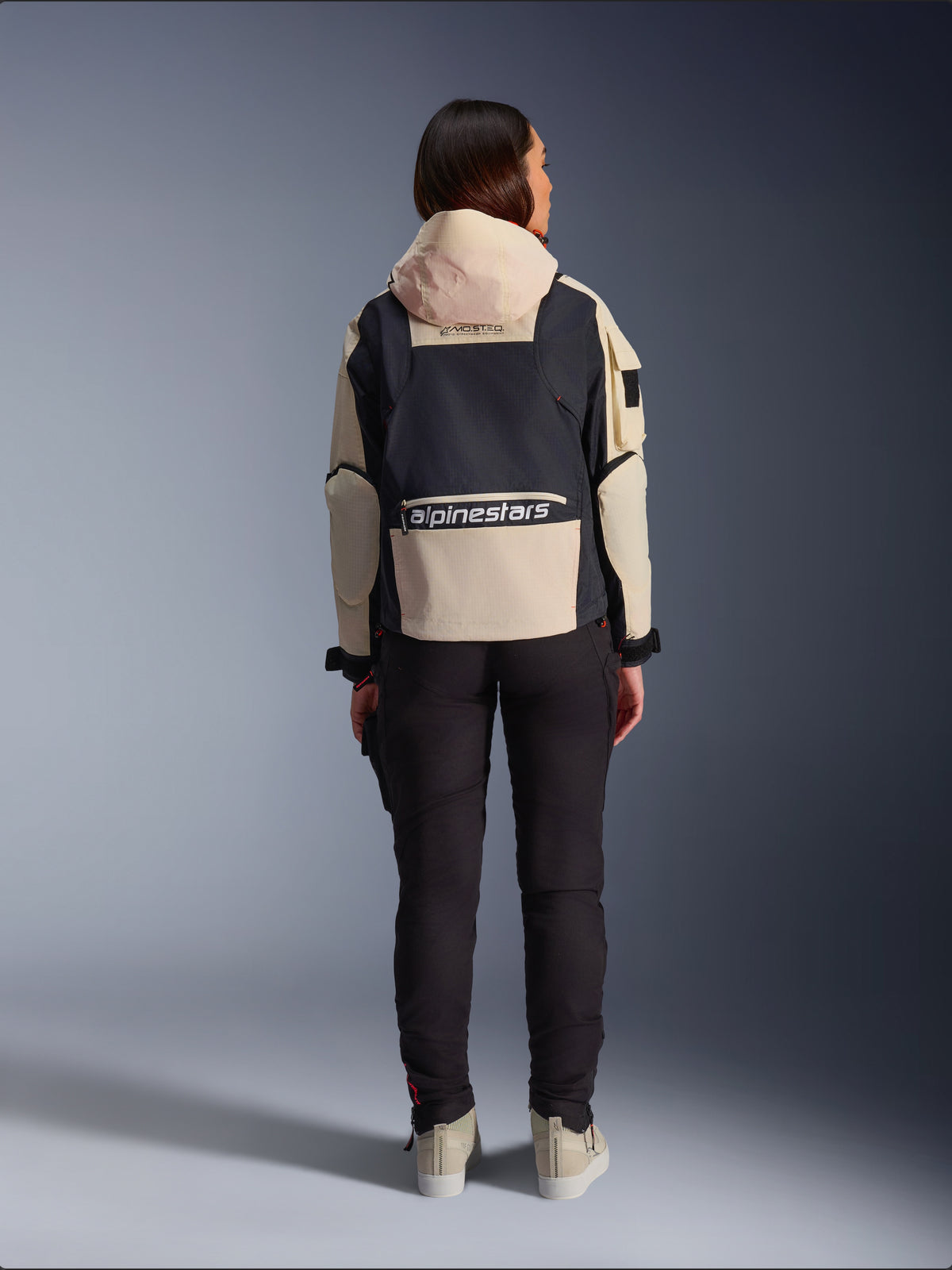 Alpinestars Molly Air Jacke, Damen-Motorradjacke, Black Almond, Rückansicht mit Kapuze und großem Logo auf dem Rücken, Utility-inspiriertes Ripstop-Design, kombiniert mit einer schwarzen Motorradhose.