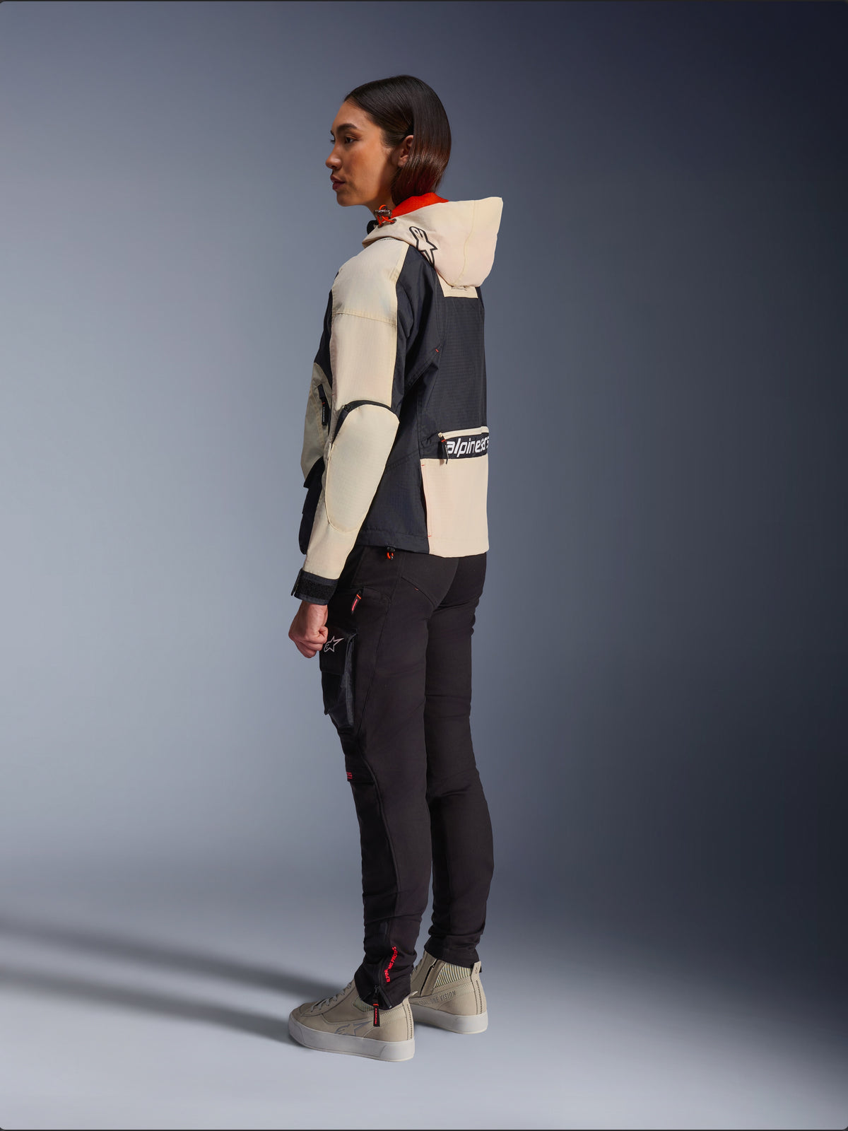 Alpinestars Molly Air Jacke, Damen-Motorradjacke, Black Almond, Design mit Kapuze, cremefarbenen Ärmeln und schwarzem Torso, kombiniert mit schwarzer Motorradhose und beigen Sneakern, urbaner zeitgenössischer Stil.