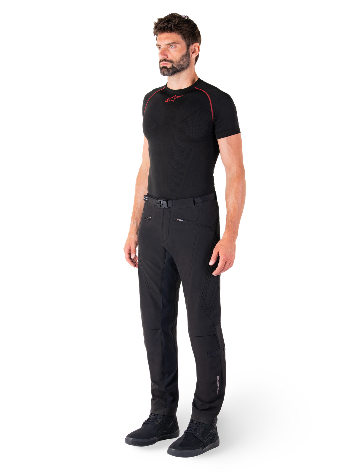 Alpinestars Alden Hose, Urbane Motorradhose, Schwarz, Softshell-Textil in regulärer Passform, getragen von einem Model mit schwarzem Base-Layer und Motorradschuhen, mit Taillengürtel mit Magnetverschluss und Reißverschlusstaschen.