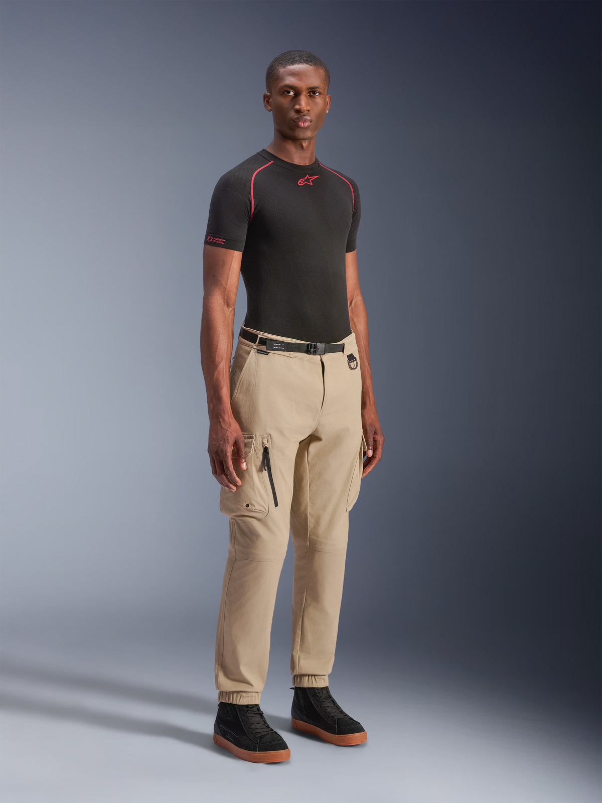 Alpinestars Flex-AST Cargo-Hose – Short, hellbeige urbane Motorradhose, getragen von einem Modell mit schwarzem Baselayer und Sneakern, reguläre Tapered-Passform, elastische Säume und Multi-Pocket-Cargo-Design