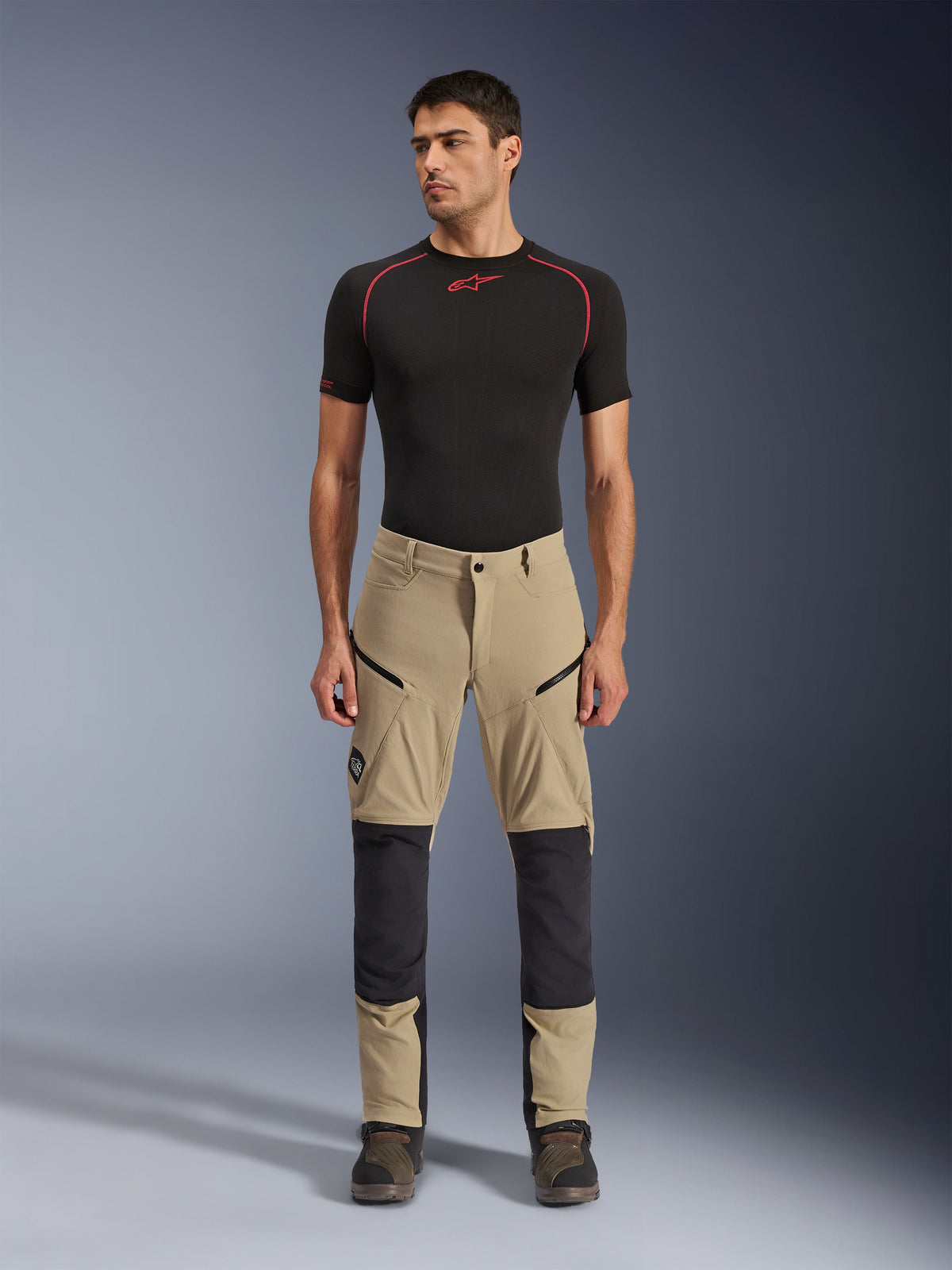 Alpinestars Flex-AST Explorer Hose, Motorrad-Abenteuerhose, Beige und Schwarz, mit verstärkten Kniepanelen, Cargotaschen mit Reißverschluss und Ripstop-Konstruktion, getragen von einem Model in einer Frontansicht im Studio.