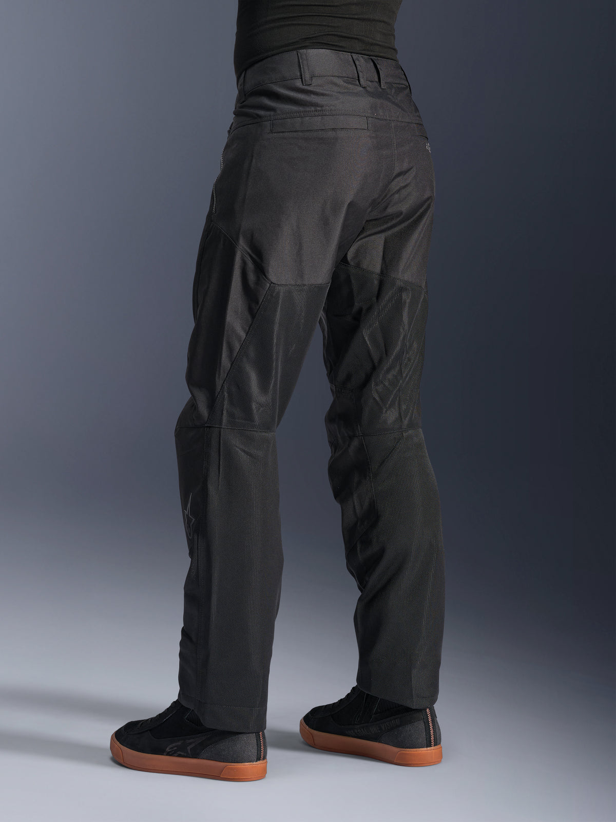 Alpinestars C-1 Air Hose, Urbane Motorradhose, Schwarz, Rückansicht mit großen Tech-Mesh-Einsätzen an der Beinrückseite zur Belüftung, schlichtes Design für die Stadt, getragen mit lässigen schwarzen Sneakern.