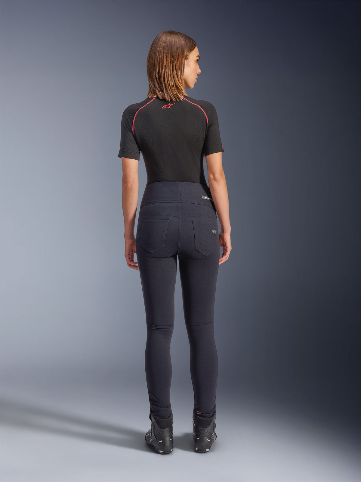Alpinestars Stella Flex-AST Leggings in Schwarz, hoch taillierte Damen-Motorradhose, Rückansicht mit Skinny-Passform und Gesäßtaschen, getragen mit schwarzem Kurzarm-Oberteil und Motorradstiefeln, urbane Fahrausrüstung