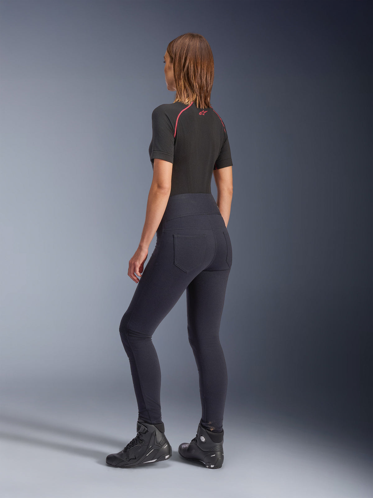 Alpinestars Stella Flex-Ast Damen-Leggings, Schwarz, Rückansicht mit hoch taillierter Passform und Gesäßtaschen, getragen mit schwarzem kurzärmeligem Baselayer mit roten Akzenten und schwarzen Motorradschuhen, moderne urbane Motorradausrüstung