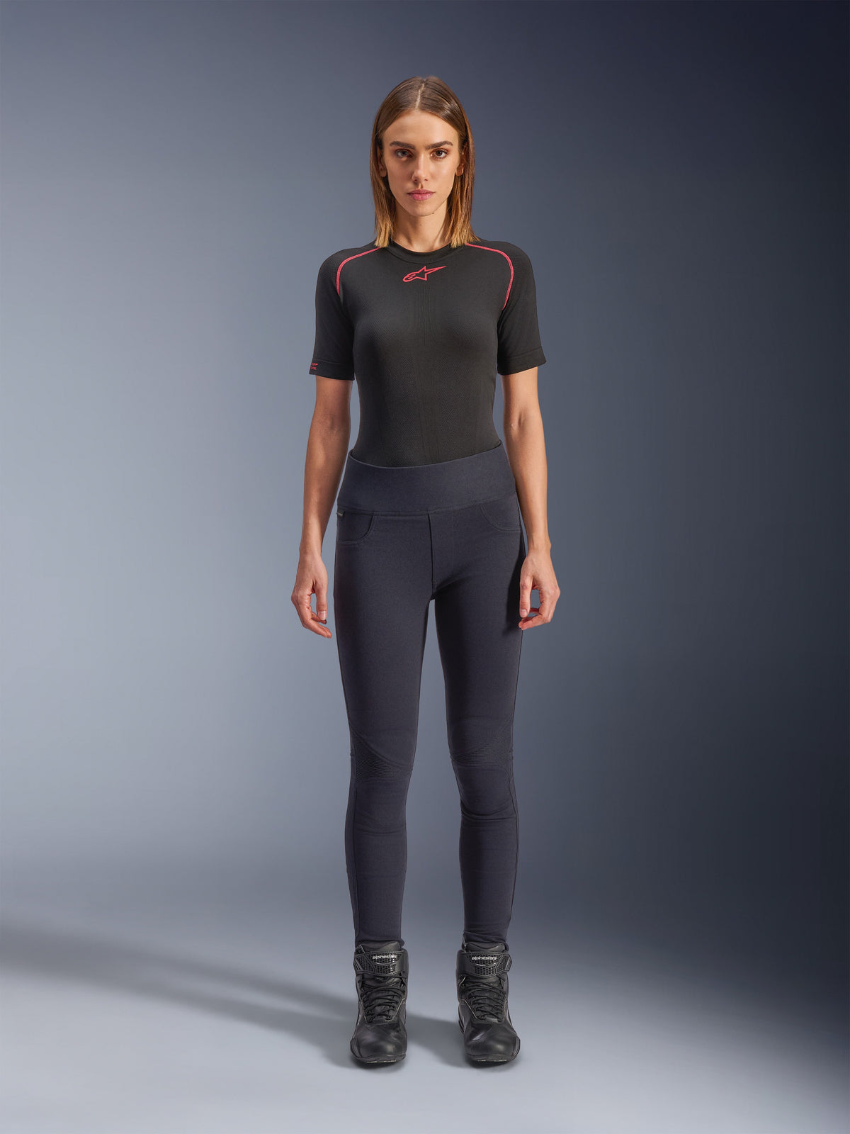 Alpinestars Stella Flex-Ast Leggings, Damen-Motorrad-Leggings, Schwarz, getragen mit einem schwarzen kurzärmeligen Oberteil mit roten Details und schwarzen Motorradstiefeln, moderne urbane Fahrausrüstung in Slim-Fit-Passform, Vorderansicht