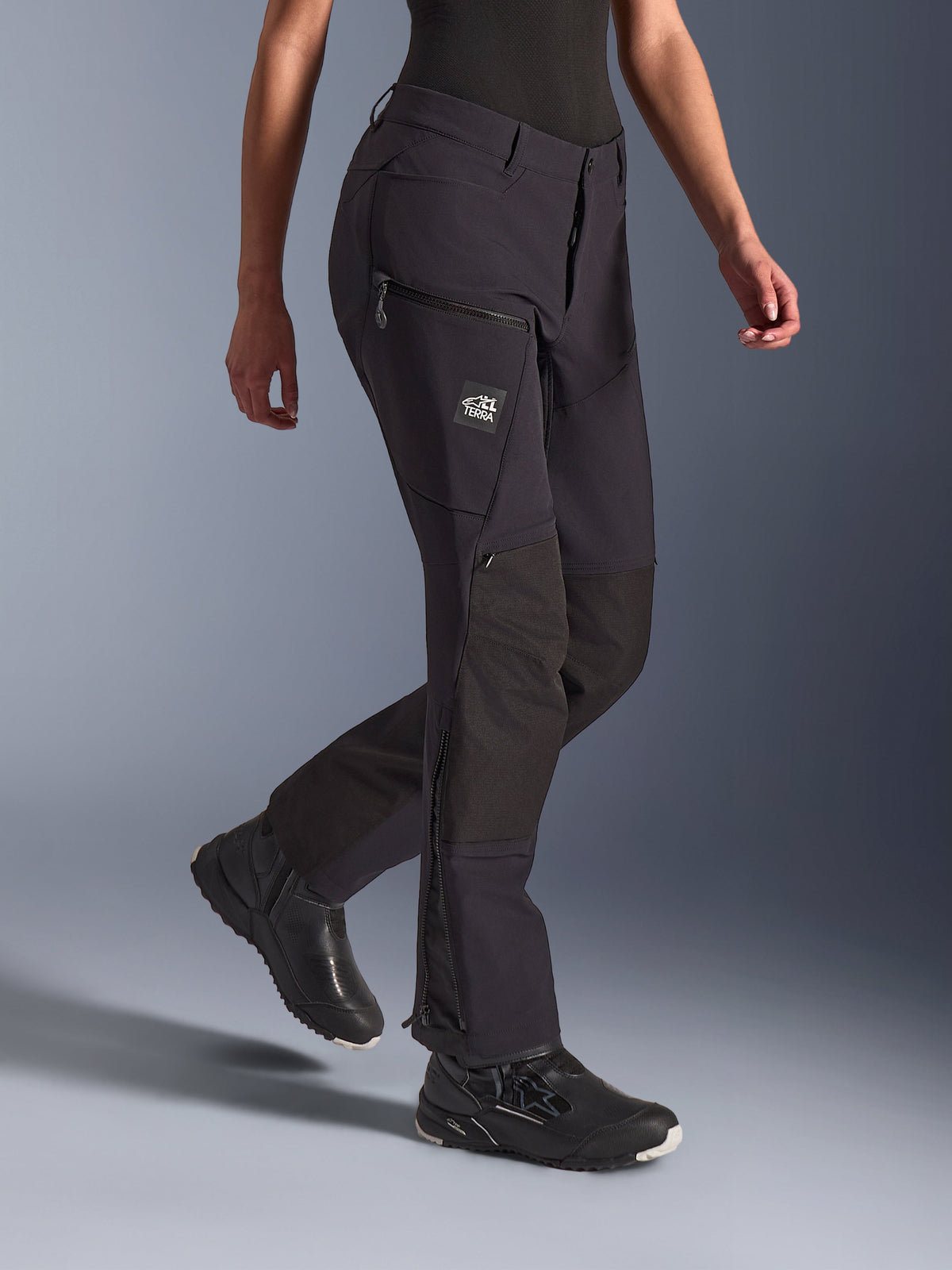 Alpinestars Woman Stella Flex-AST Explorer Pants, Black, Adventure Motorcycle Pants, featuring stretch textile construction with ripstop knee reinforcements, zippered cargo pockets with TERRA branding, and lower leg zippers, worn with black riding footwear.