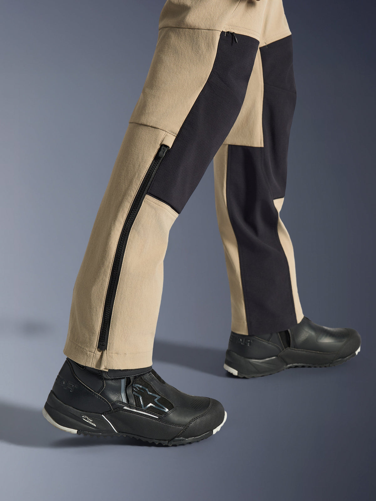 Alpinestars Stella Flex-AST Explorer Damenhose, Motorrad-Abenteuerhose, Sand und Schwarz, Nahaufnahme der Unterschenkel und Knöchel mit langem seitlichem Reißverschluss und schwarzen Verstärkungspanelen, getragen mit schwarzen Alpinestars Motorradschuhen.