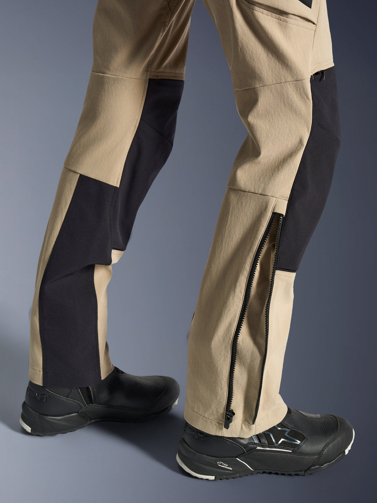 Alpinestars Stella Flex-AST Explorer Hose, Damen-Motorradhose, Sand und Schwarz, Nahaufnahme der unteren Hosenbeine mit Reißverschluss am Saum für die Stiefelanpassung, kombiniert mit schwarzen Alpinestars Motorradschuhen, aus strapazierfähigem Ripstop-Gewebe und atmungsaktiven Stretch-Einsätzen.