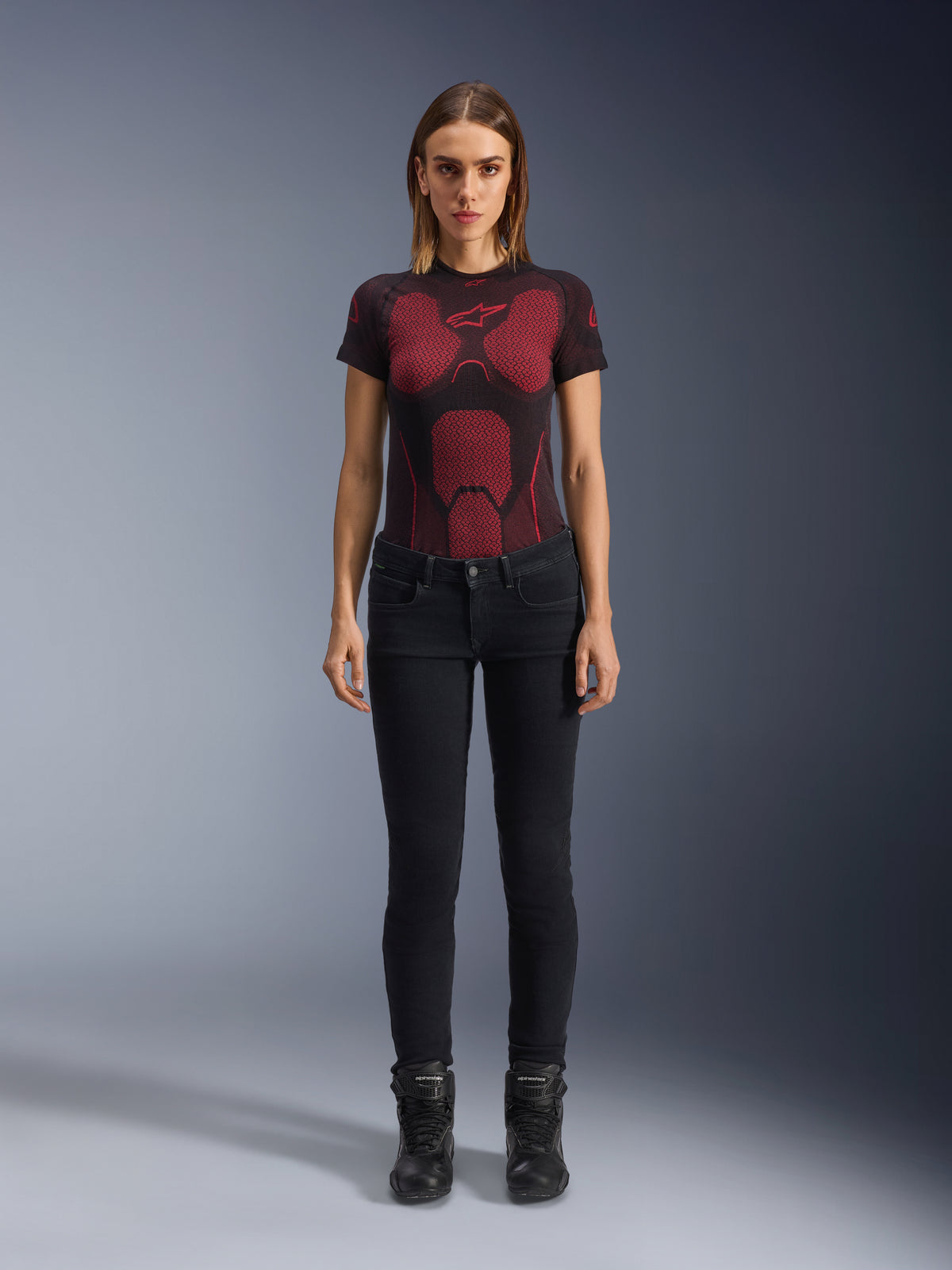 Alpinestars Daisy V3 Women's Riding Denim, Rinse Black, Slim-fit Motorcycle Pants, worn by a model with a red and black patterned technical t-shirt and black motorcycle boots, casual urban riding gear with a feminine silhouette and high-waisted design.