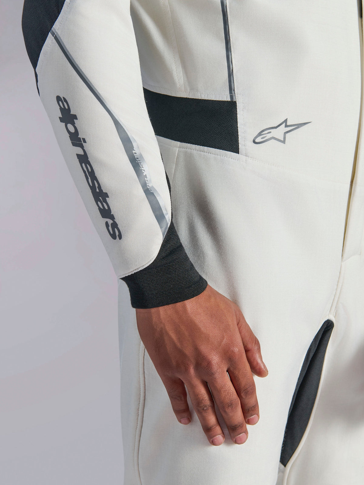 Alpinestars Hypertech V3 Anzug, Nahaufnahme eines weißen Auto-Rennanzugs mit schwarzen und silbernen Akzenten, Alpinestars-Logo auf dem Unterarm, schwarzes Strickbündchen und dunkle Stretcheinsätze für Bewegungsfreiheit, professionelle Motorsportbekleidung