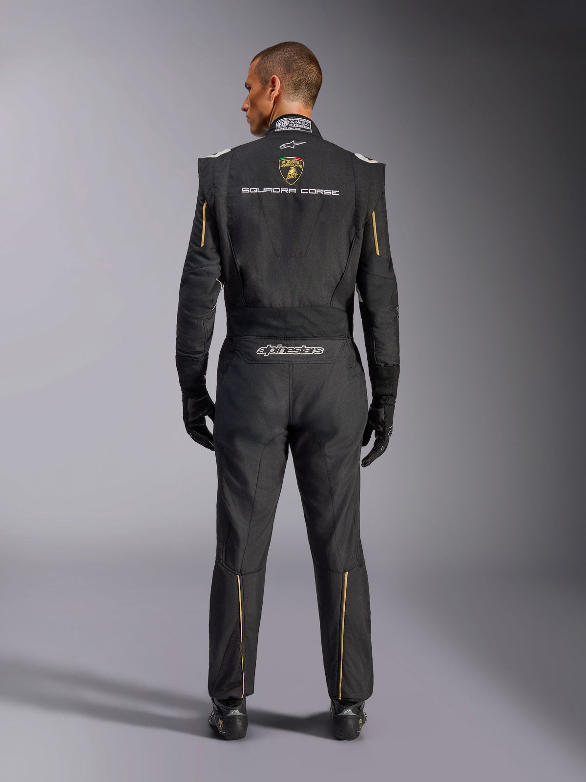 Alpinestars Limitierte Edition Lamborghini GP Tech V4 Anzug FIA, Automobil-Rennanzug, Schwarz mit gold- und silberfarbenen Akzenten, Rückansicht mit Lamborghini Squadra Corse Branding, Alpinestars-Logo und goldener Paspelierung an Ärmeln und Beinen, professionelle Rennausrüstung