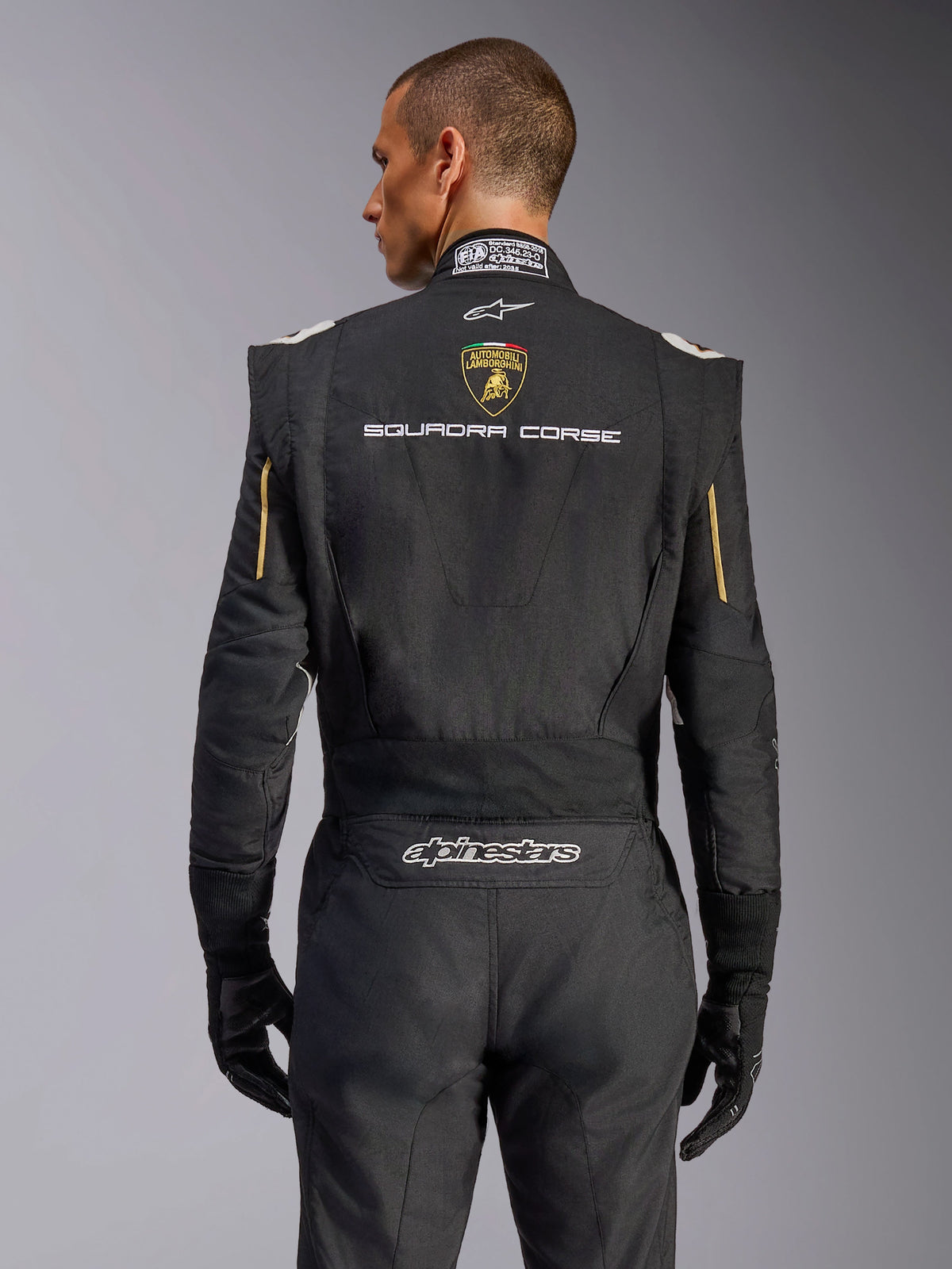Rückansicht des Alpinestars Limited Edition Lamborghini GP Tech V4 Anzugs, Schwarz mit Gold-Akzenten, mit Automobili Lamborghini Wappen und „SQUADRA CORSE“-Schriftzug auf dem Rücken, professioneller FIA-zertifizierter Rennanzug für den Automobilsport