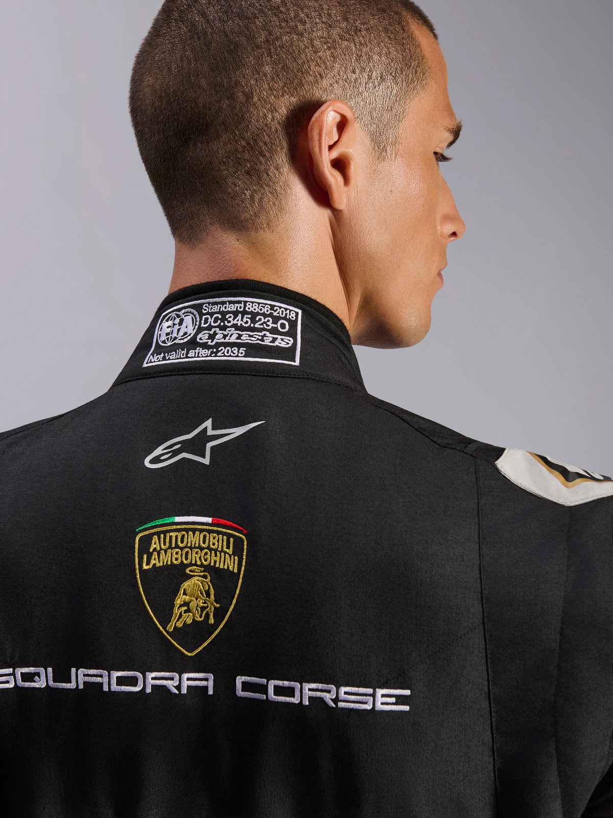 Alpinestars Limited Edition Lamborghini GP Tech V4 Anzug FIA, Nahaufnahme des oberen Rückens und Kragens, schwarzer Anzug mit Automobili Lamborghini-Wappen und Squadra Corse-Stickerei, Alpinestars-Logo und FIA 8856-2018 Zertifizierungsetikett am Kragen.