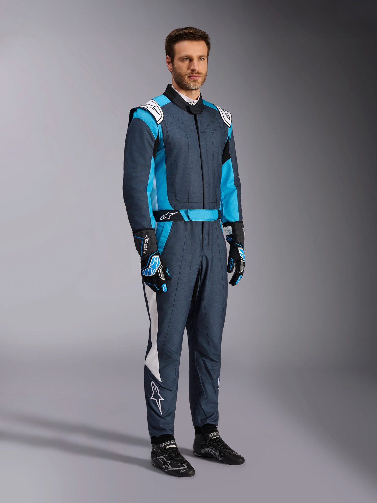 Alpinestars GP Pro Comp V2 Kombi, FIA Auto-Rennanzug für Herren in Asphalt und Cyan, getragen von einem Model.