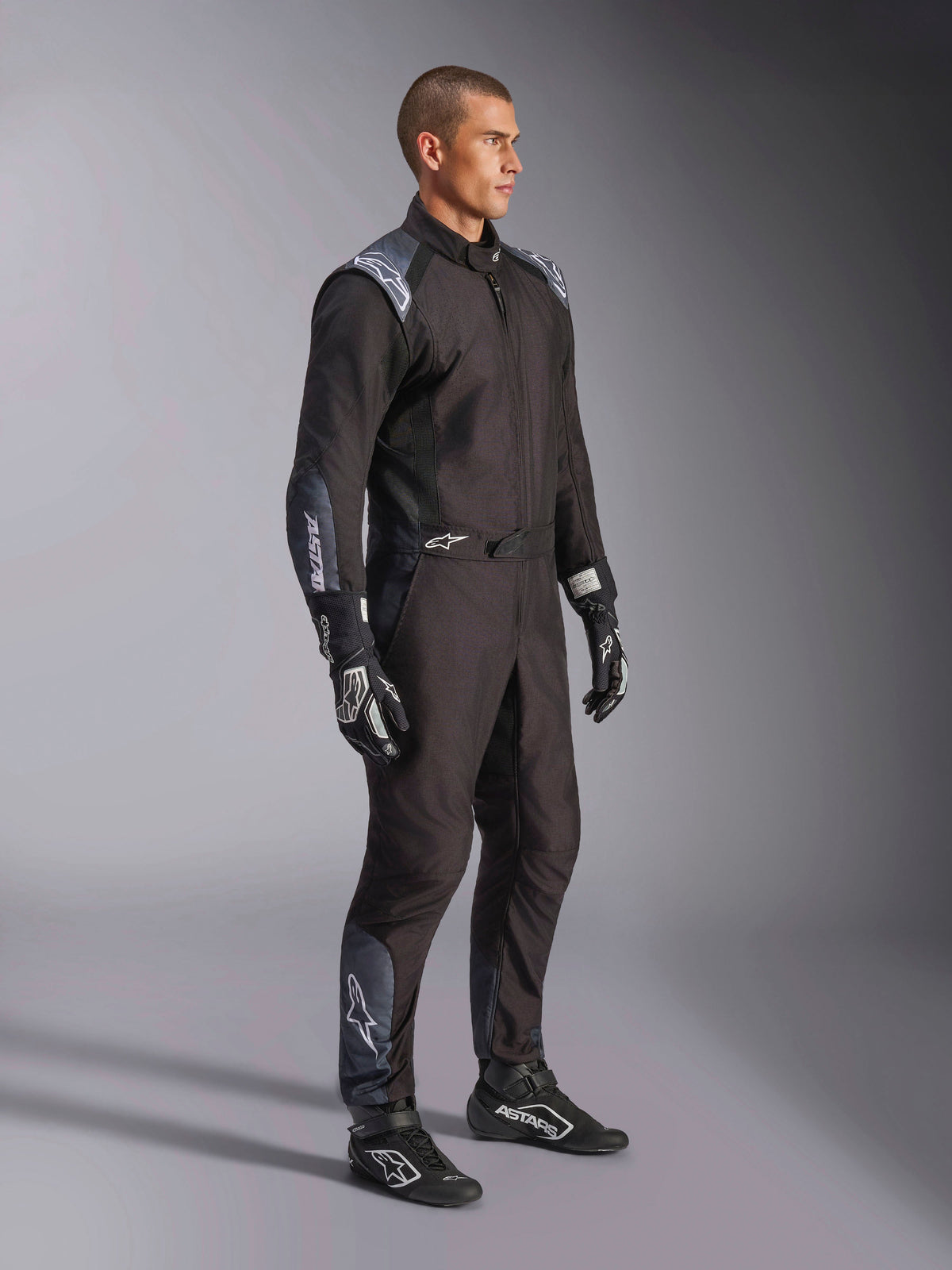 Alpinestars KMX-5 V3 Anzug, Kart-Anzug in Black Dark Shadow, getragen mit passenden schwarzen Rennhandschuhen und Schuhen, mit lasergeschnittenen Perforationen und Tech-Mesh-Einsätzen, elegantes zweilagiges Design mit weißem Branding für den professionellen Motorsport