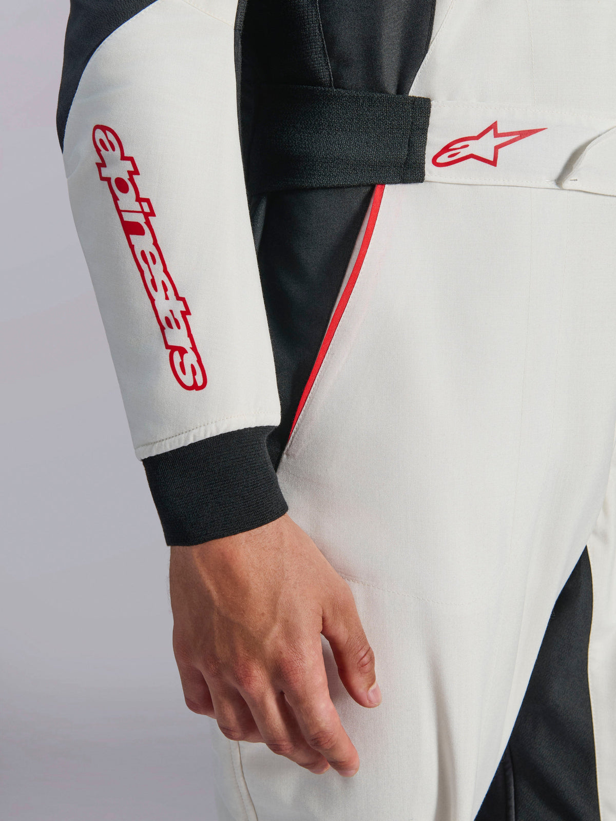 Alpinestars GP Tech V4 Suit, White Black Red Auto Racing Suit, close-up of the sleeve and waist, featuring red Alpinestars wordmark and star logo, elastic waist with hook-and-loop closure, and red accent piping on white and black technical fabric