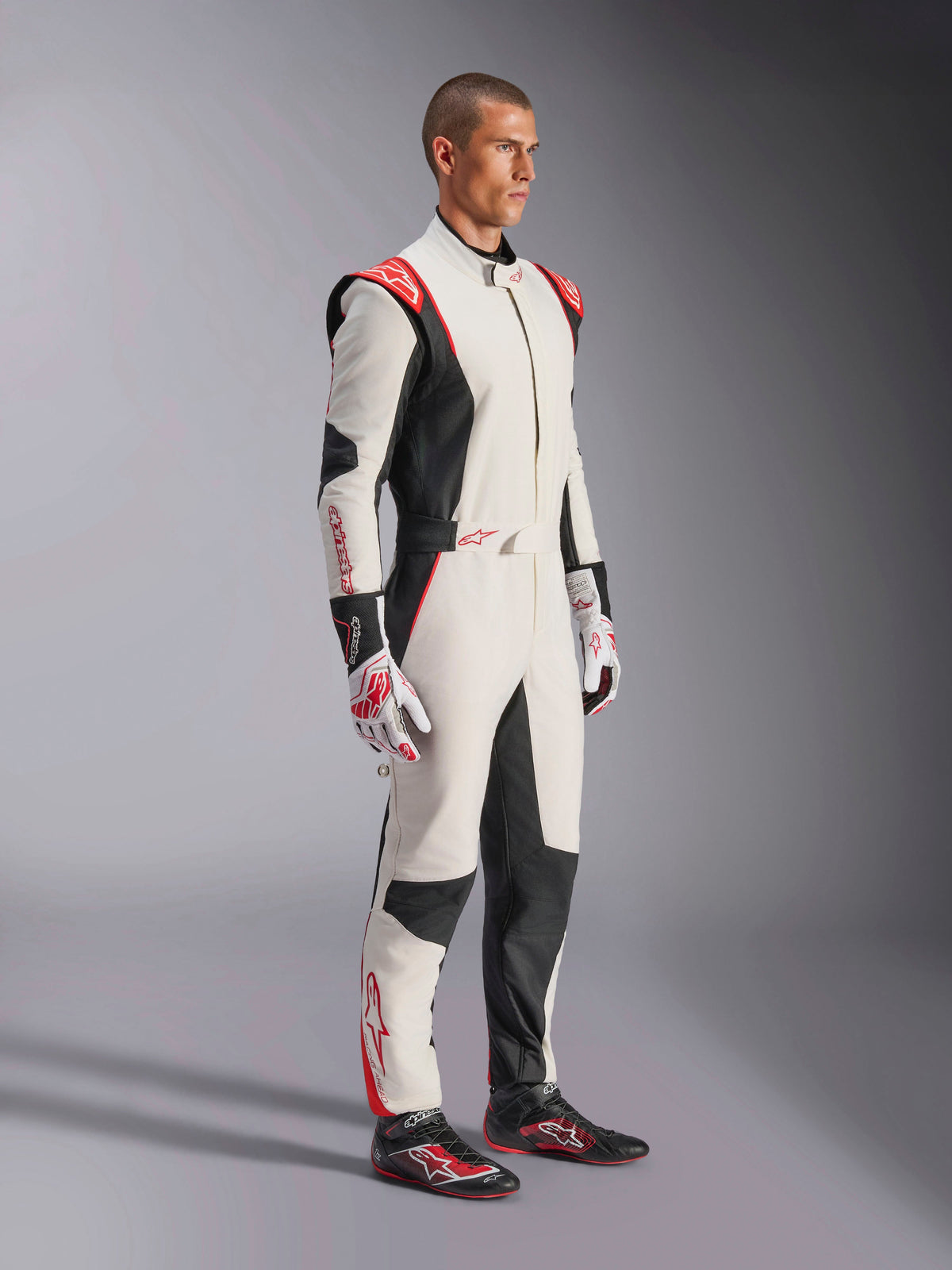 Male racing driver wearing Alpinestars GP Tech V4 Suit, White Black and Red, full-length one-piece auto racing suit, matching gloves and racing shoes, professional motorsport gear with Alpinestars branding and ergonomic design