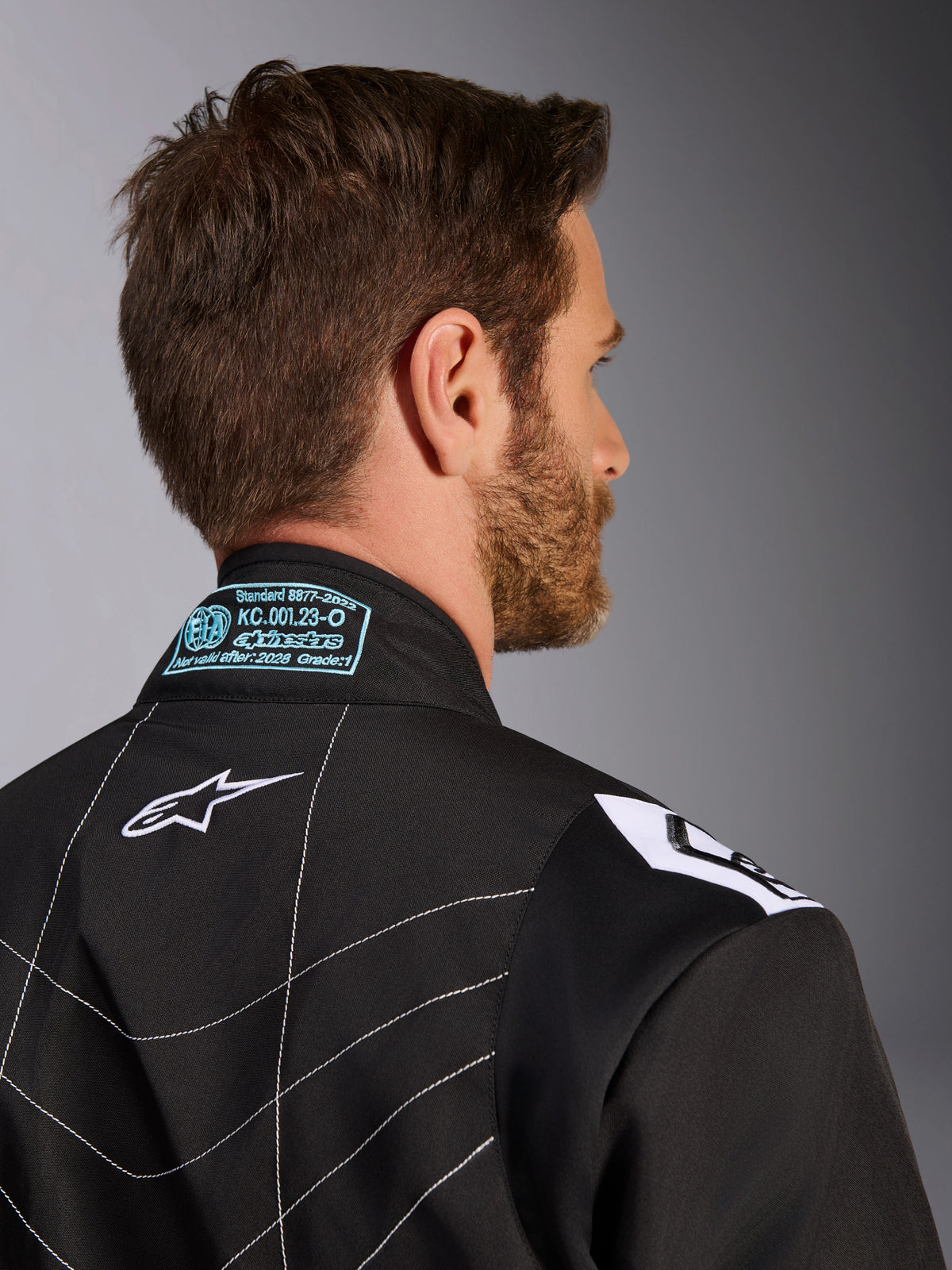 Alpinestars KMX-9 V3 Anzug, Schwarz und Weiß, Nahaufnahme des hinteren Kragens und des Schulterbereichs, mit hellblau gestickten FIA-Homologationsdetails, weißem Stern-Logo und weißen Kontrastnähten.