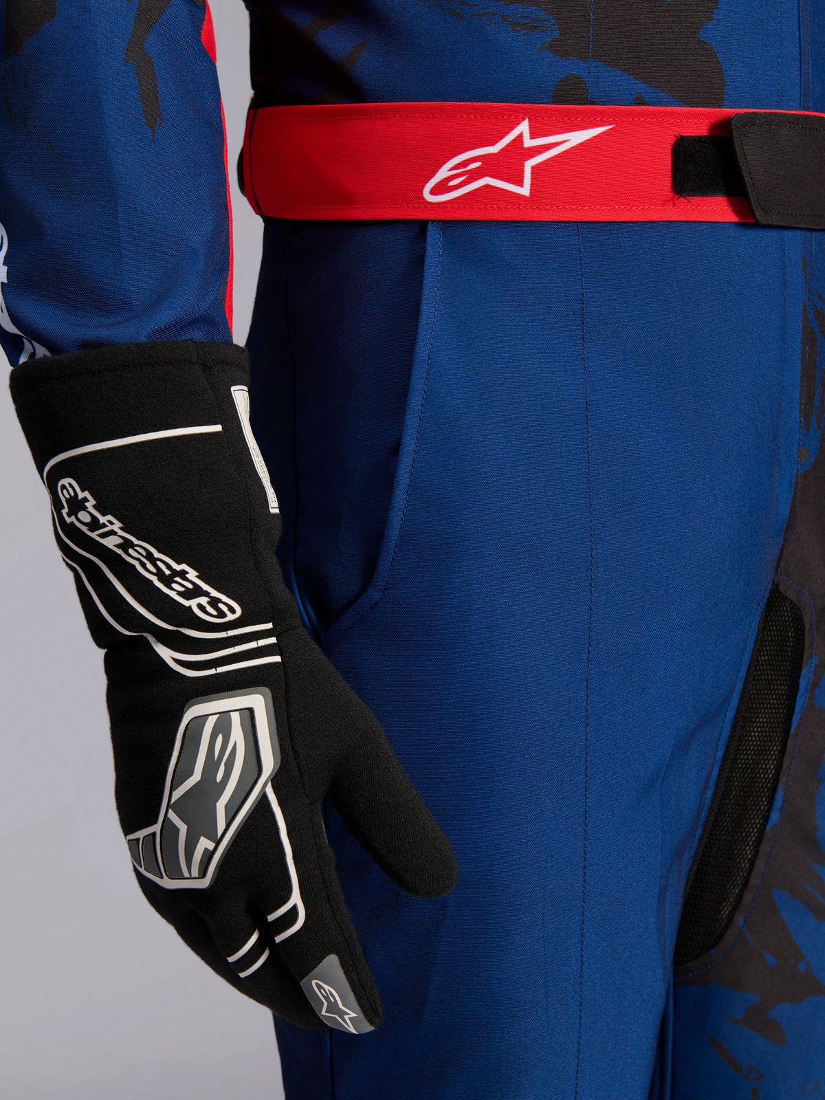 Alpinestars KMX-9 V3 Graphic 5 Anzug, Kart-Anzug, Navy und Rot, Nahaufnahme des roten verstellbaren Taillengürtels mit weißem Logo, getragen mit schwarzem Kart-Handschuh, strapazierfähiger navy-farbener Stoff und integrierte Oberschenkeltasche