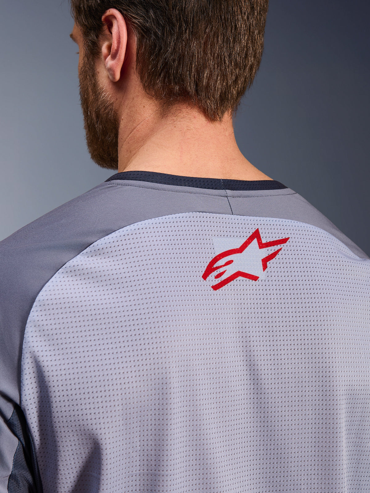 Alpinestars Maxdura Dual Jersey in Mid Gray und Dark Gray, Nahaufnahme des oberen Rückens und Kragens, mit einem kleinen roten Alpinestars Stern-Logo auf atmungsaktivem, hellgrauem Mesh-Gewebe mit dunkelgrauem Kragenbesatz, entwickelt für Adventure-Offroad-Fahrten