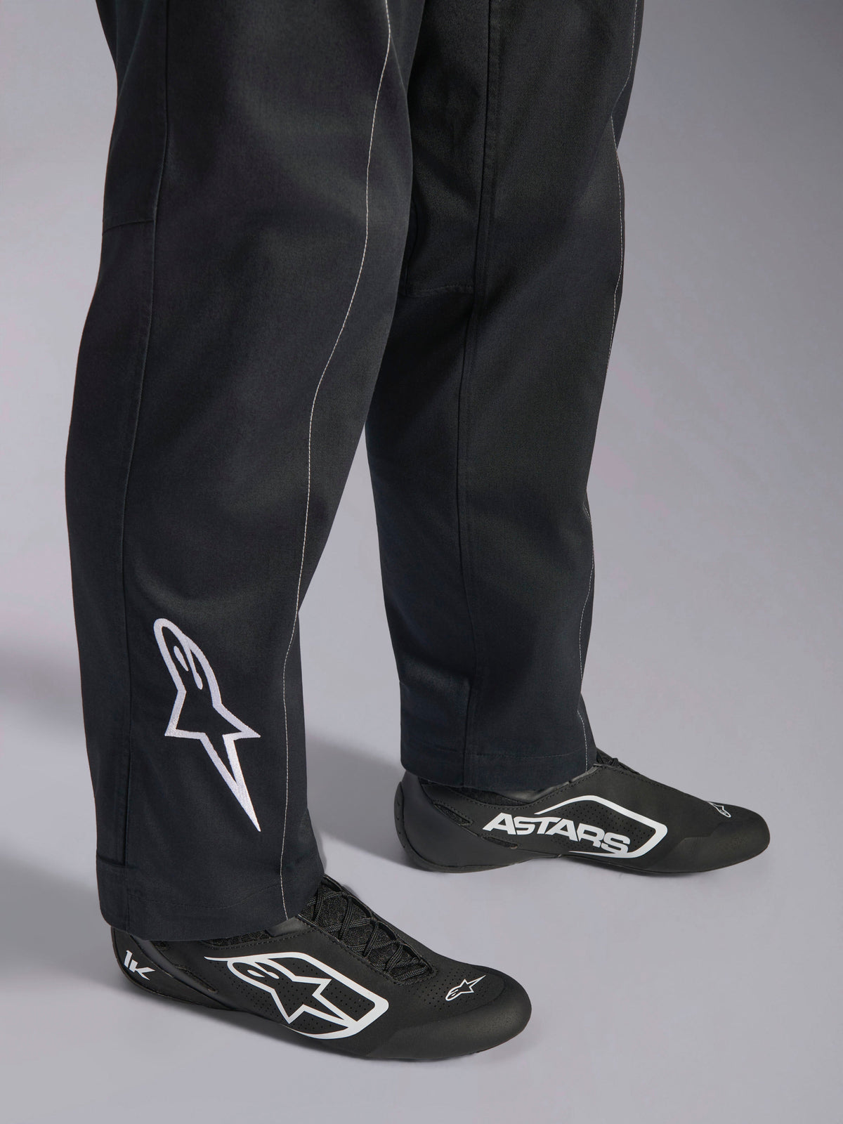 Alpinestars Kart Indoor V2 Anzug, schwarzer Kart-Anzug, Nahaufnahme der Unterschenkel und Füße mit weißem Alpinestars-Logo an der Wade, kombiniert mit passenden schwarz-weißen Rennschuhen, konzipiert für das Freizeit-Kartfahren.