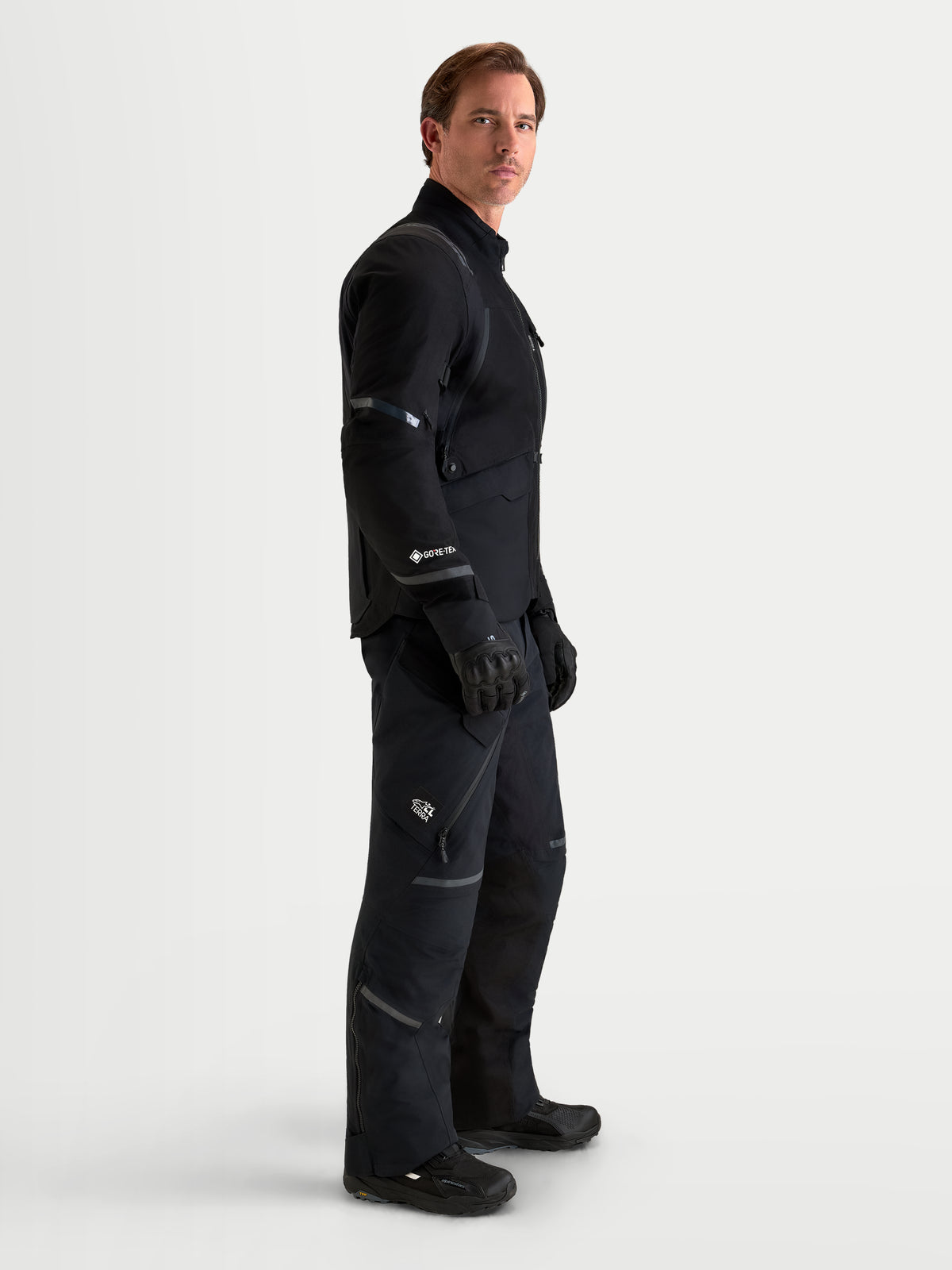 Alpinestars St-7 V2 2L Gore-Tex Jacket and St-7 V2 2L Gore-Tex Pants, men's black adventure touring motorcycle gear set, side-profile studio shot worn by a model featuring waterproof 2L laminated GORE-TEX and CE-certified protection