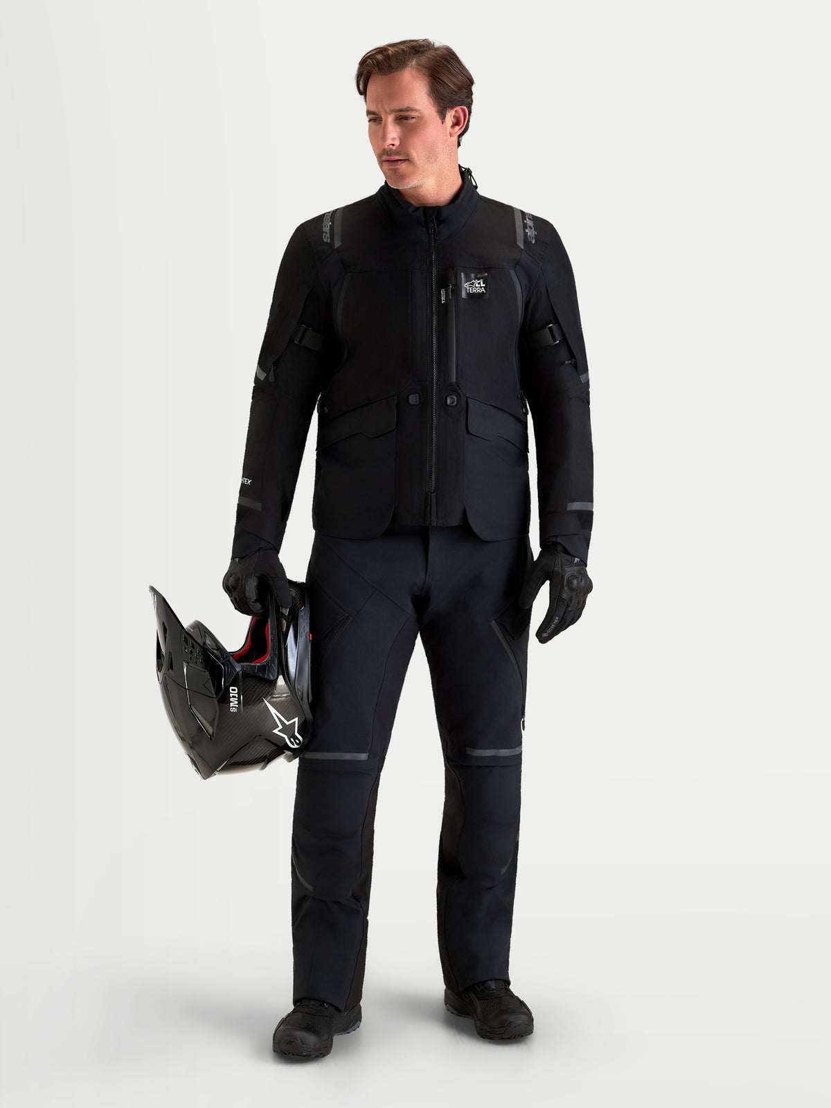 Alpinestars St-7 V2 2L Gore-Tex Jacket, men's black adventure motorcycle touring jacket, featuring a waterproof GORE-TEX shell and direct ventilation, worn by a model holding a black helmet and matching black gear