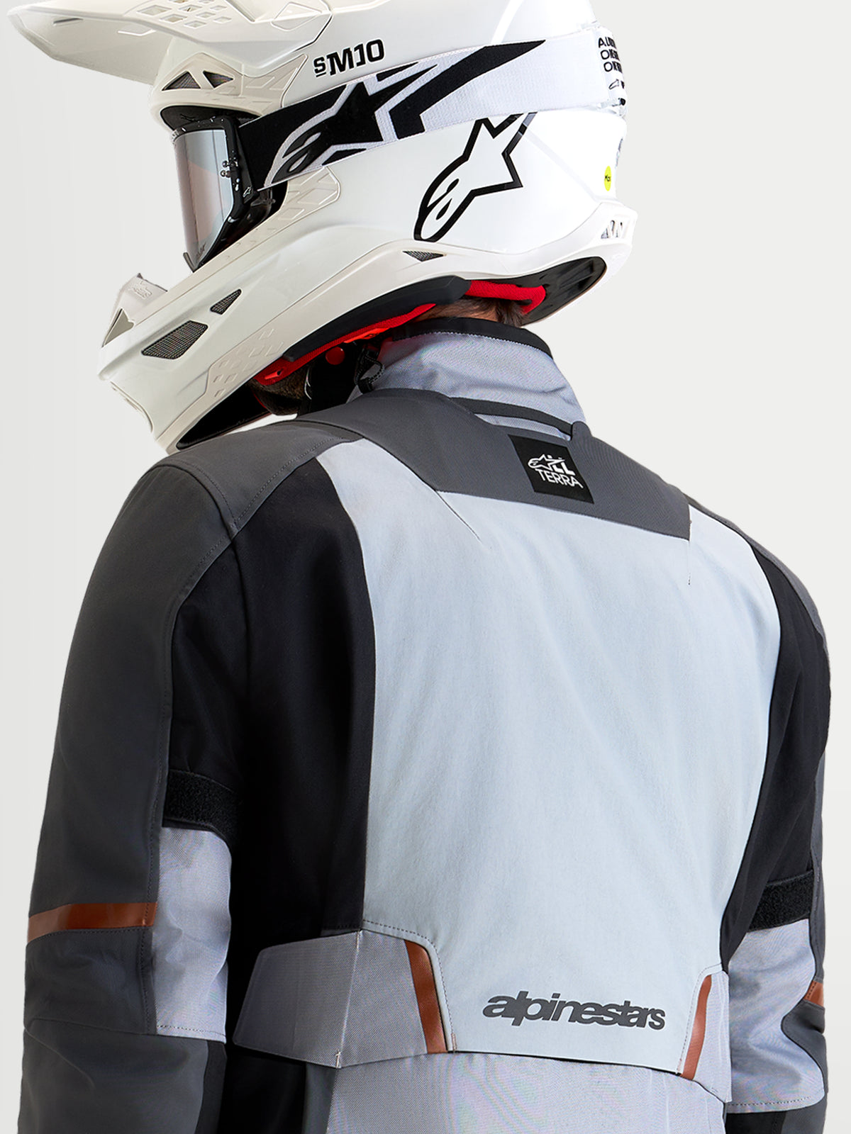 Alpinestars St-7 V2 2L Gore-Tex Jacket, Men's adventure touring motorcycle jacket in mid gray, deep gray, and black, rear view showing a rider wearing a white off-road helmet and waterproof textile construction with stretch panels