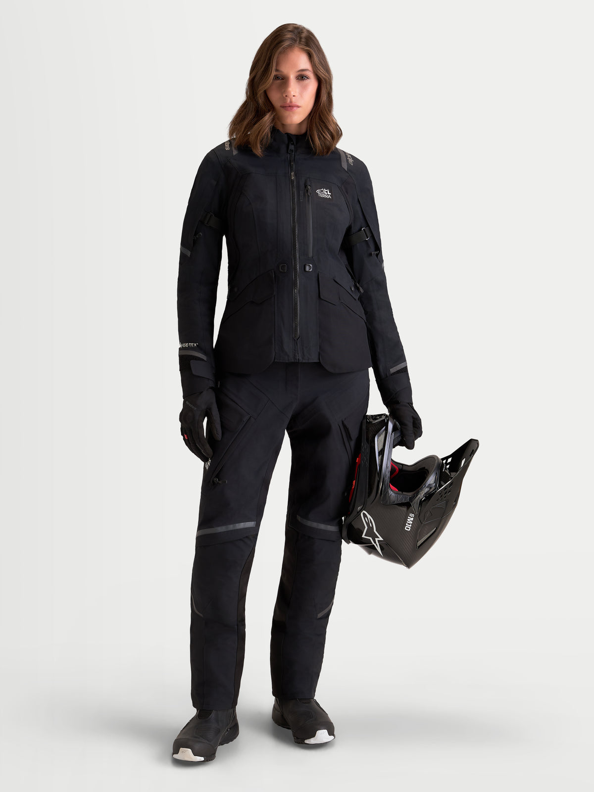 Alpinestars Stella ST-7 V2 2L GORE-TEX Jacket, women's adventure touring motorcycle jacket in black, full-length view on a model wearing matching gear and holding a helmet, waterproof textile construction with CE-certified protection.