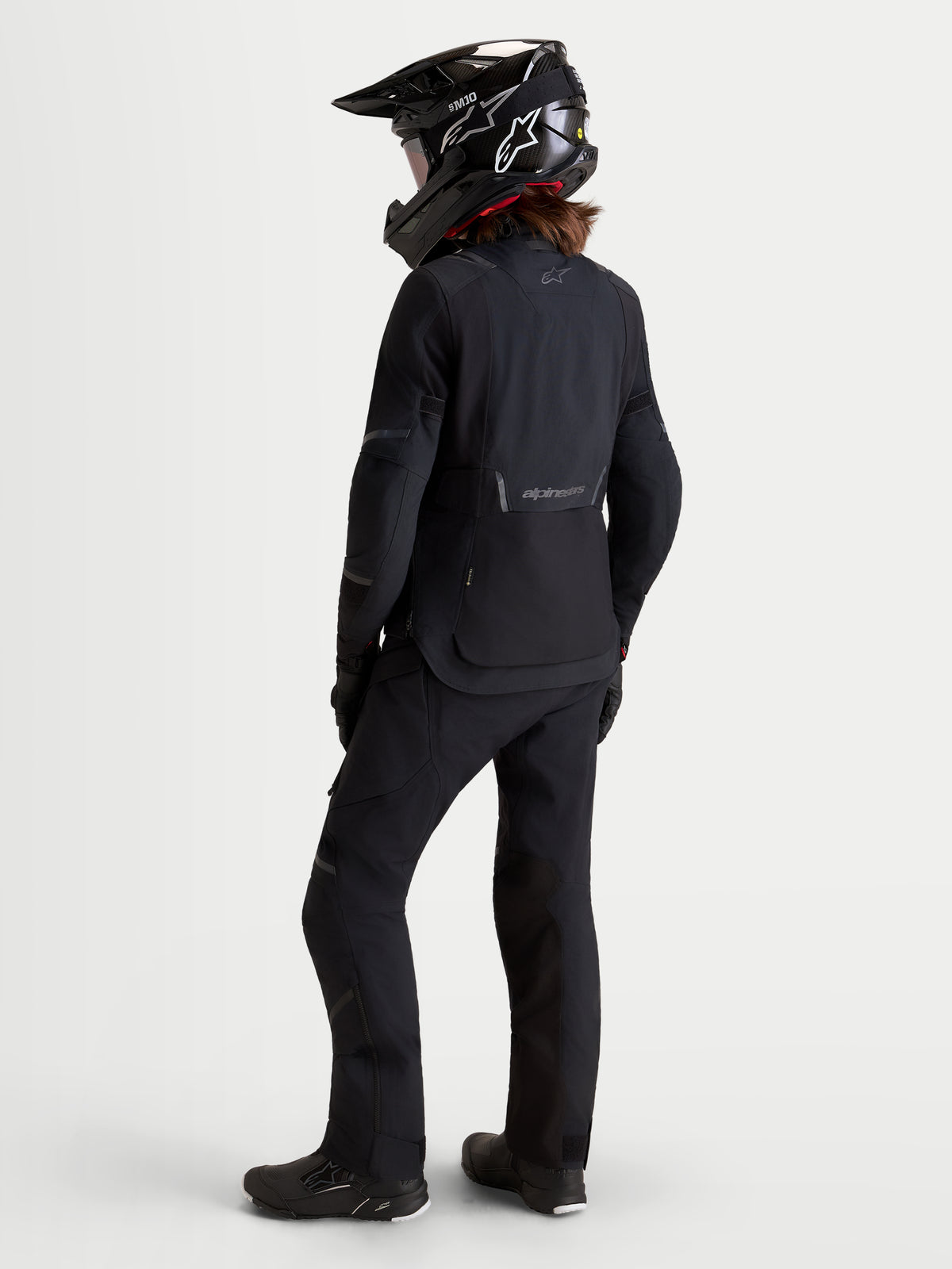 Alpinestars Stella ST-7 V2 2L Gore-Tex Jacket, women's adventure touring motorcycle jacket in black, rear three-quarter view on a model wearing matching gear and helmet, waterproof textile construction.