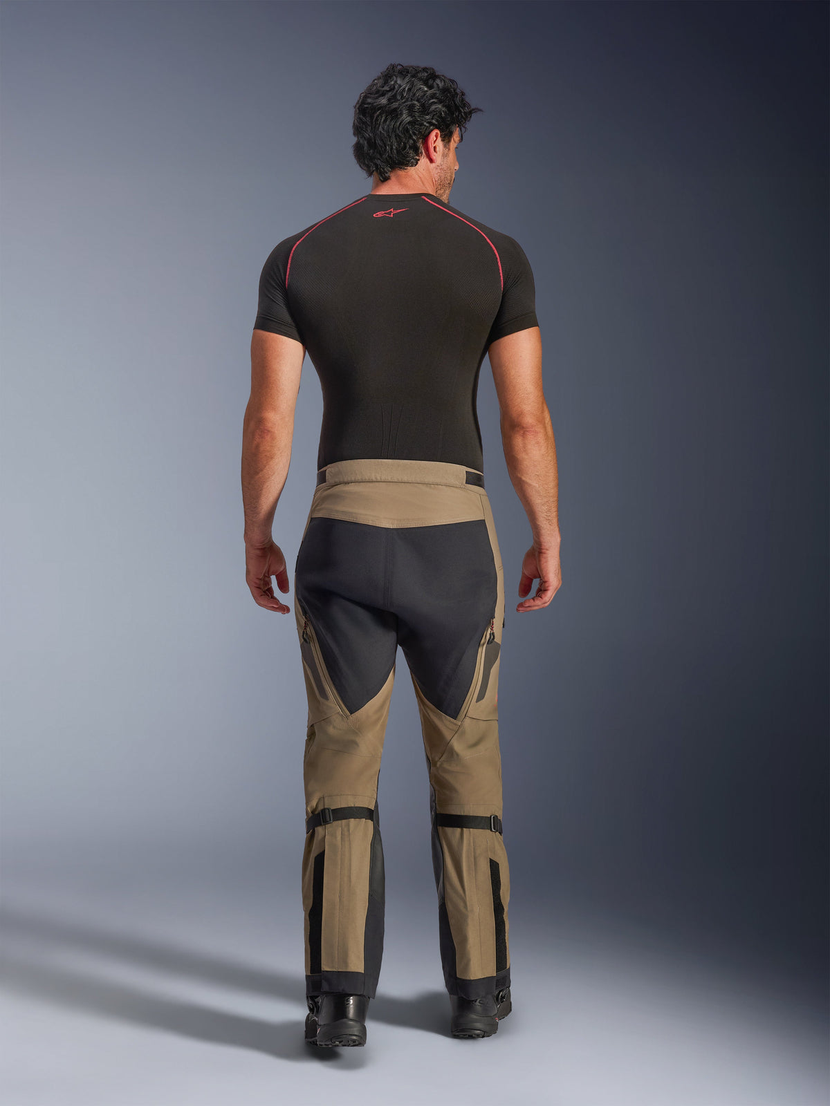 Alpinestars Nazca 3L GORE-TEX PRO Pants, Walnut Black adventure motorcycle pants, rear view on a model wearing a black base layer and boots, featuring a two-tone design with calf adjusters and stretch panels.