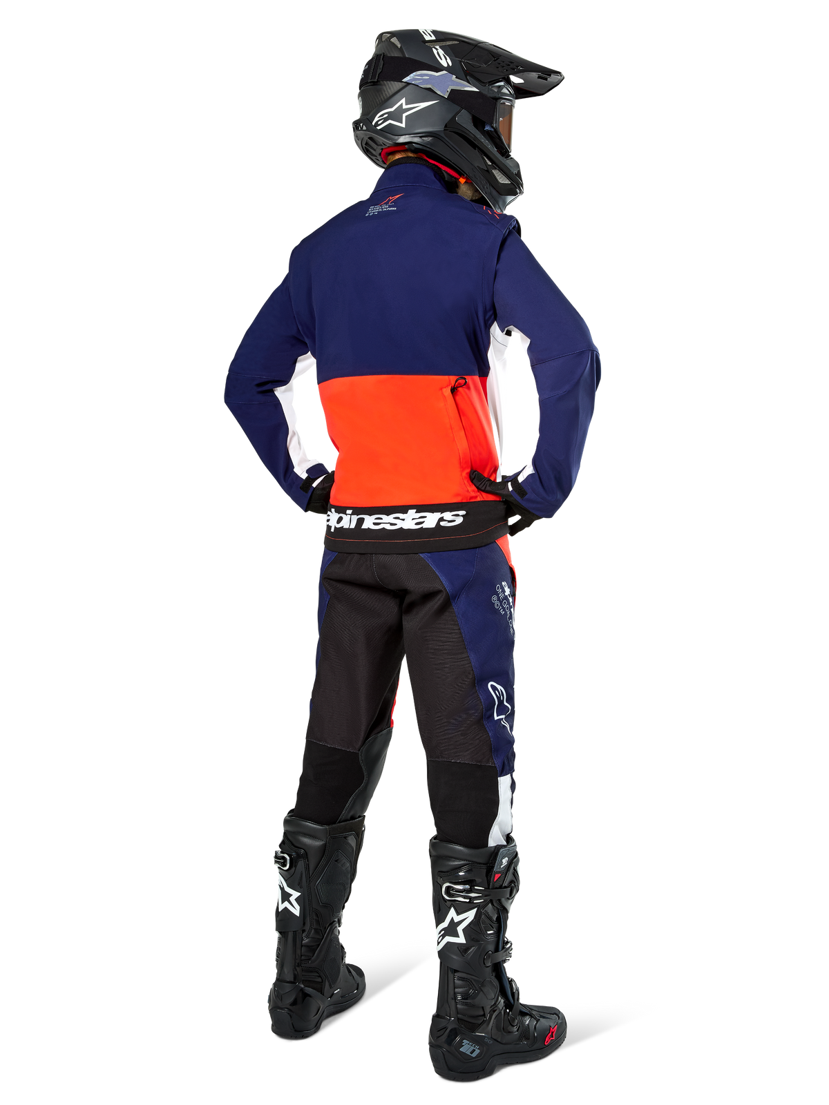 Motocross-Fahrer in der Rückansicht, trägt die Alpinestars Lite-Dura Softshell-Jacke in Navy, Hot Orange und Weiß, zeigt die große Rückentasche. Kombiniert mit einer passenden Enduro-Hose, einem schwarzen Motocross-Helm und schwarzen Offroad-Stiefeln.