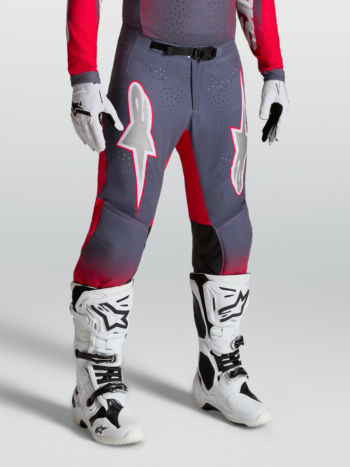 Alpinestars Supertech Hiten AFD Hose, Motocross-Hose in Grau und Rot, mit weißen Sterngrafiken und Magnetschnalle, getragen mit weißen Stiefeln.