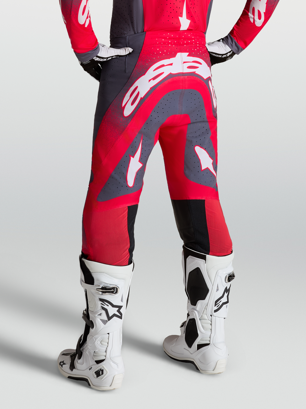 Alpinestars Supertech Hiten AFD Hose, Motocross-Hose in Rot und Grau, Rückansicht am Model mit weißen Rennstiefeln.