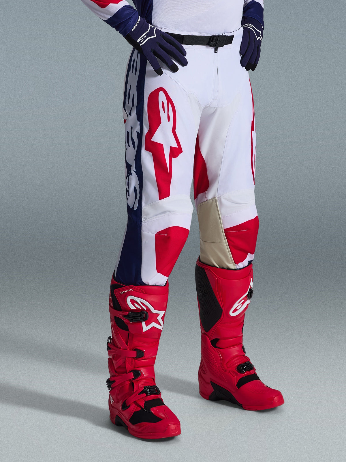 Alpinestars 2026 Racer Riway Pants, Motocross Pants, White Blue Red, featuring bold red logos on thighs and blue side panels with white branding, worn with red boots and dark blue gloves, ergonomic design for off-road racing