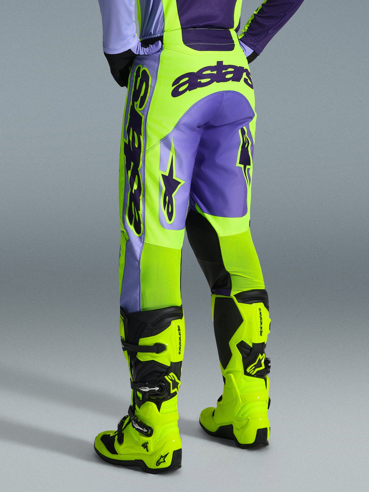 Alpinestars 2026 Racer Portl Hose, Motocross-Hose, Lila und Gelb Fluo, Rückansicht mit markantem Astars-Branding und lila Akzenten, getragen mit passenden gelben Fluo-Motocross-Stiefeln, strapazierfähiges Synthetikmaterial für den Offroad-Rennsport