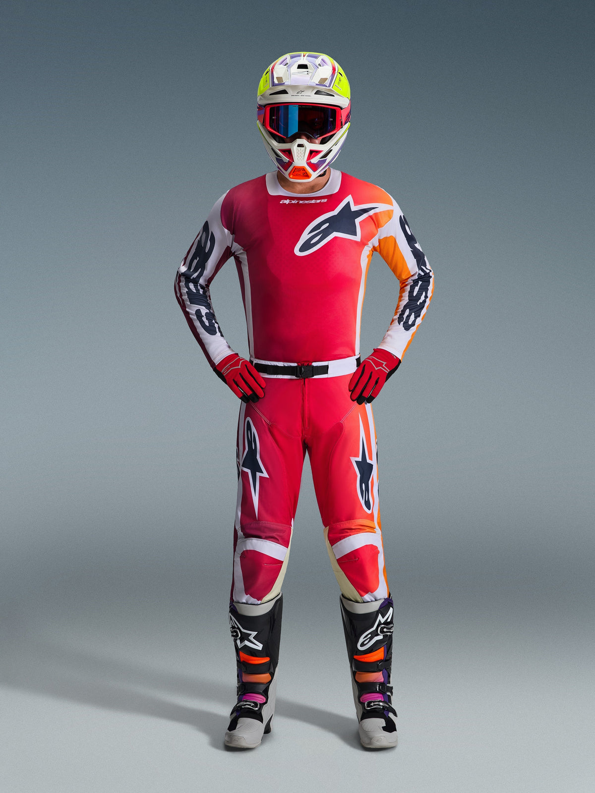Motocross-Fahrer in kompletter Rennausrüstung, rotes Trikot mit weißen und orangefarbenen Akzenten, 2026 Racer Portl Hose in Rot und Weiß, weißer Helm mit bunten Akzenten und blauer Brille, rote Handschuhe sowie schwarze und graue Stiefel, abgestimmtes Outfit für Offroad-Performance
