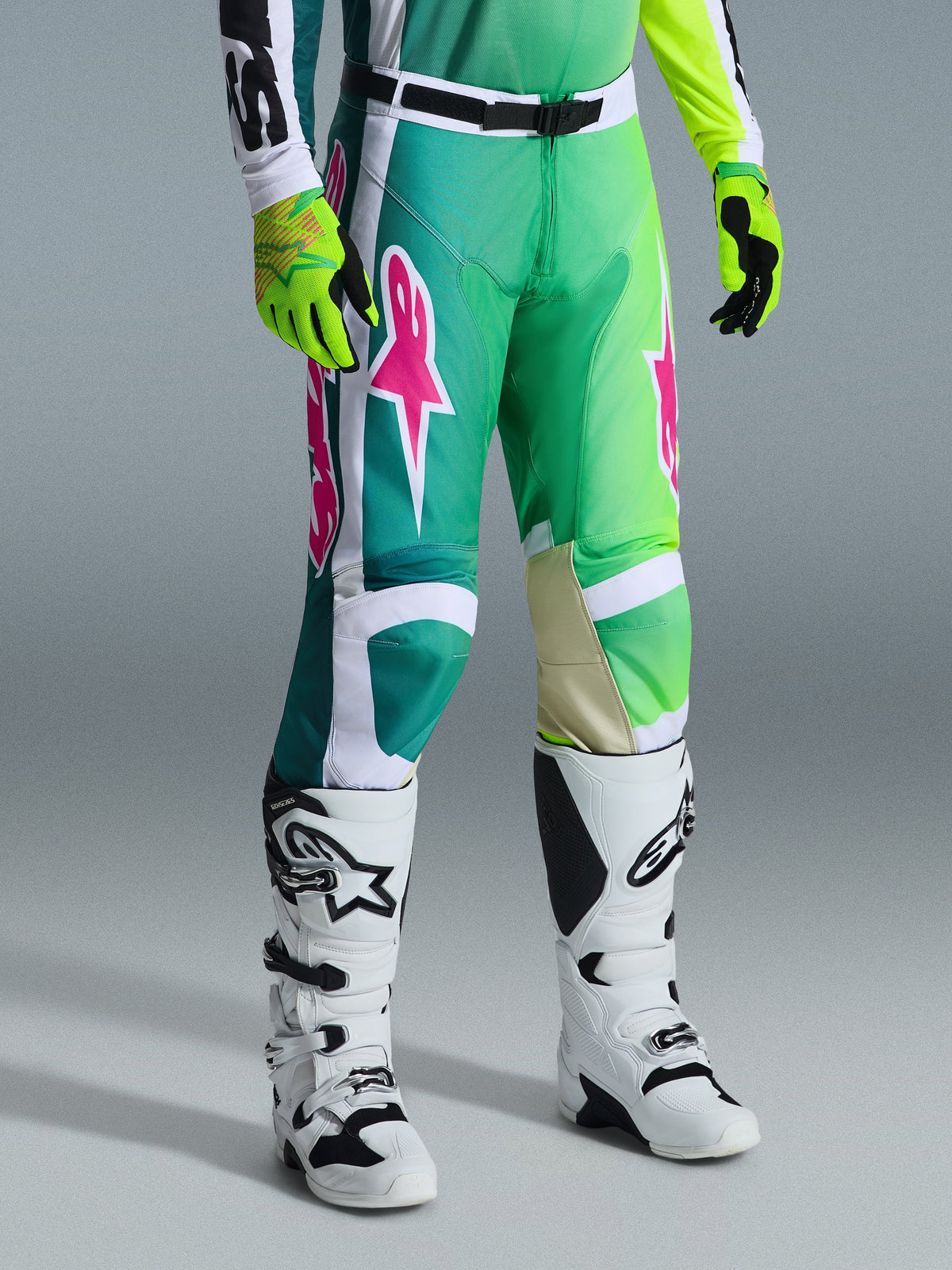 Alpinestars 2026 Racer Portl Hose, Motocross-Hose, Grün, Weiß und Schwarz mit pinkfarbenen Logos, kombiniert mit weißen Stiefeln und neongelben Handschuhen, mit auffälligen Grafikmustern und einer verstellbaren schwarzen Taillenschnalle, Performance-Ausrüstung für den Offroad-Sport